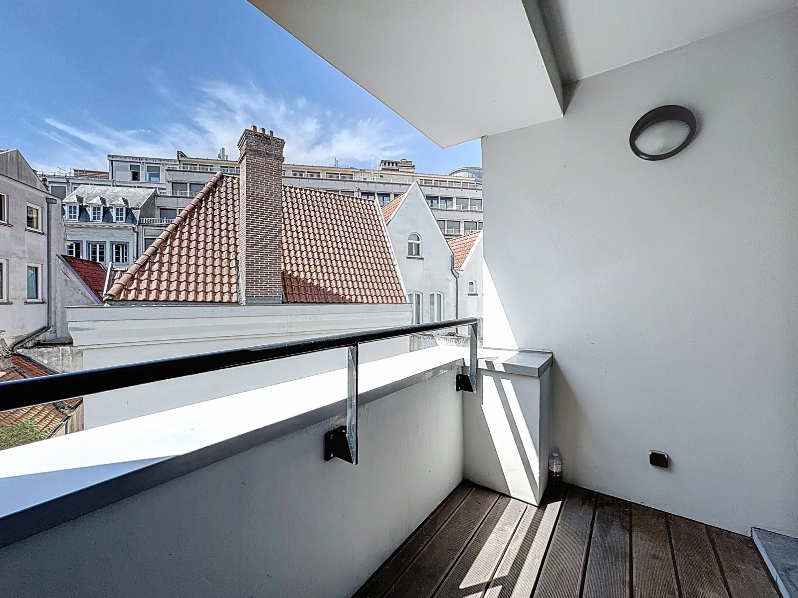 whise photo 7 Balcony with a wooden floor and white walls, overlooking red-tiled rooftops and a blue sky.