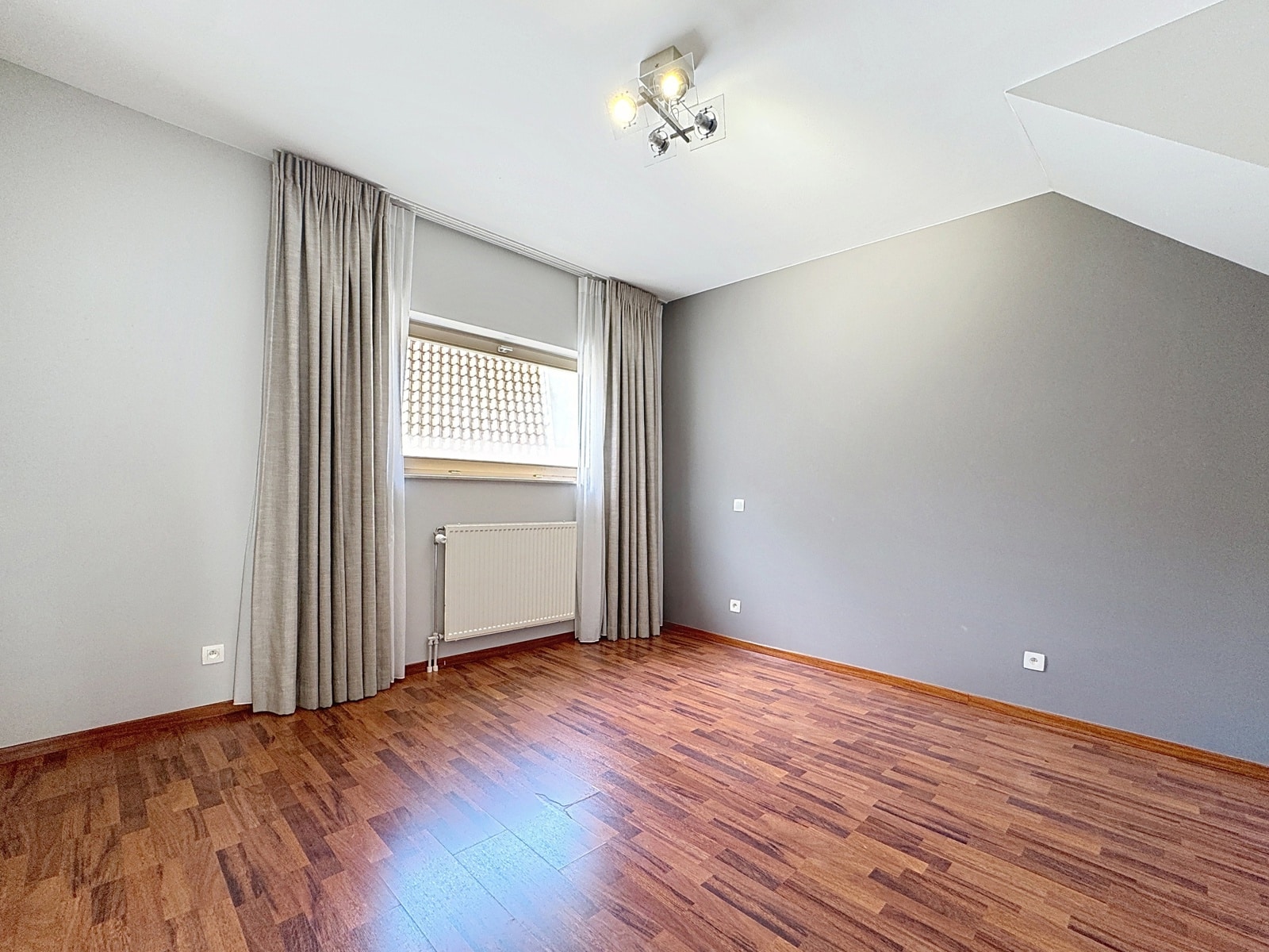 whise photo 8 Empty room with gray walls, brown wooden floor, a window with light gray curtains, and a radiator beneath.