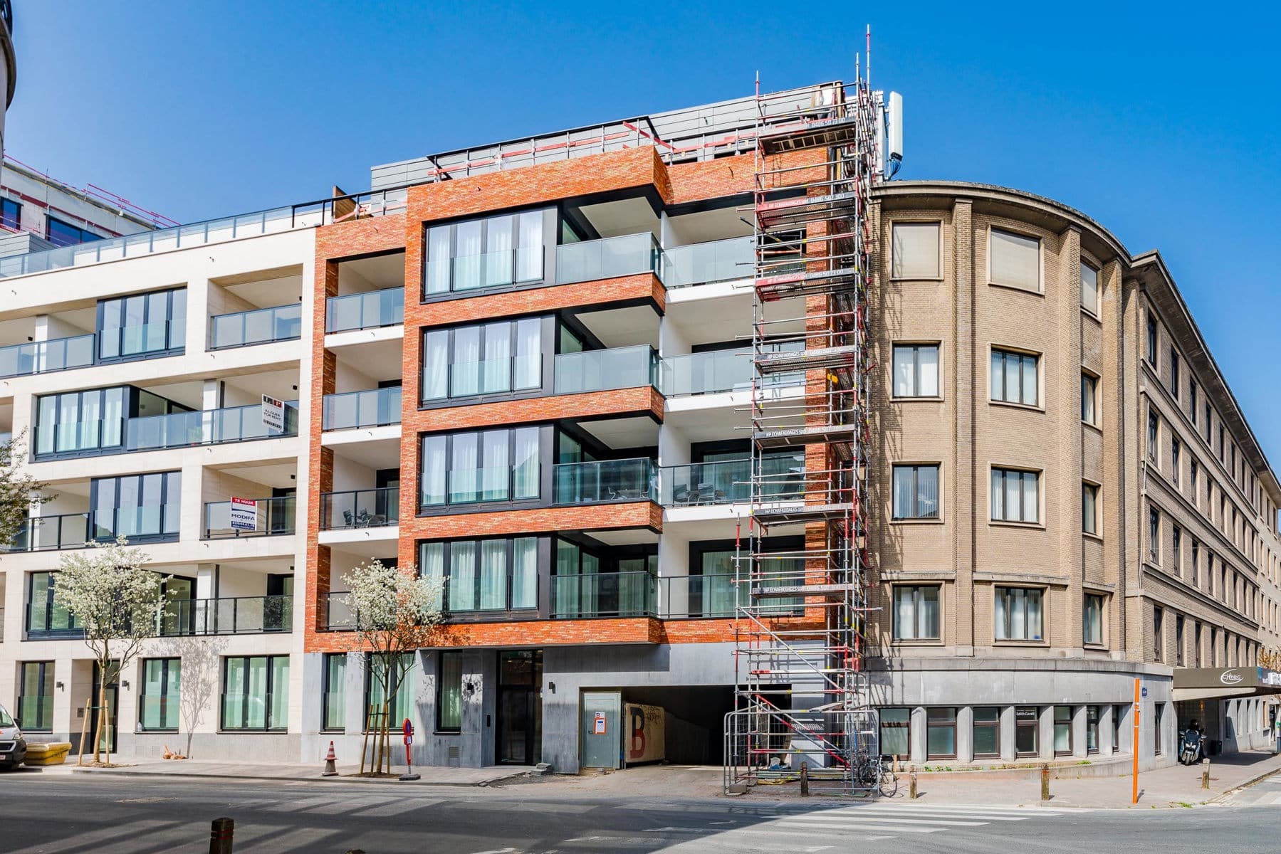 Wijze foto 10 Modern appartementencomplex met bakstenen en witte gevels onder een strakblauwe hemel; tijdens de bouw staat er aan de rechterkant een steiger.