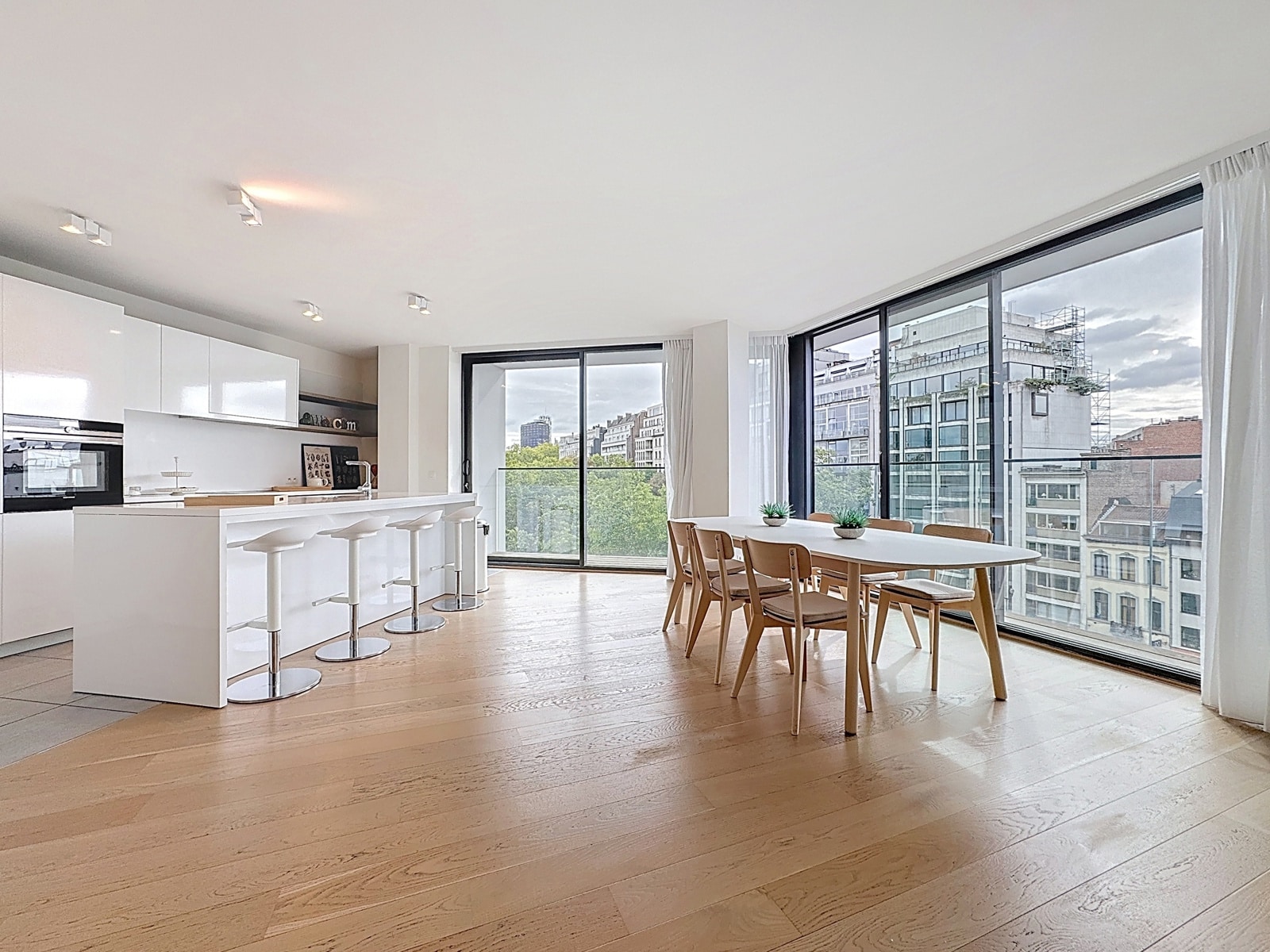 Open Kitchen with Dining Area – You Real Estate Agency Appartement lumineux avec cuisine ouverte, coin repas et grandes fenêtres.