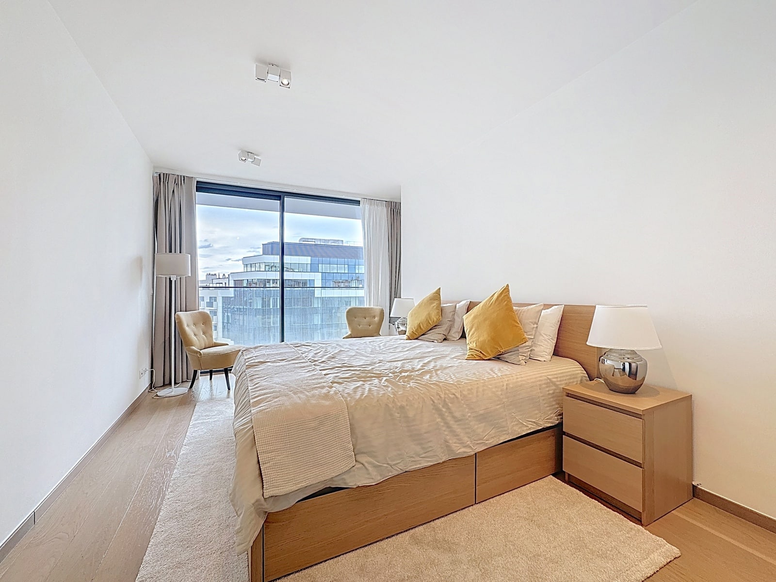 Chambre Lumineuse Avec Baie Vitrée – You Real Estate Agency Chambre lumineuse d’appartement moderne avec lit en bois et grande baie vitrée.