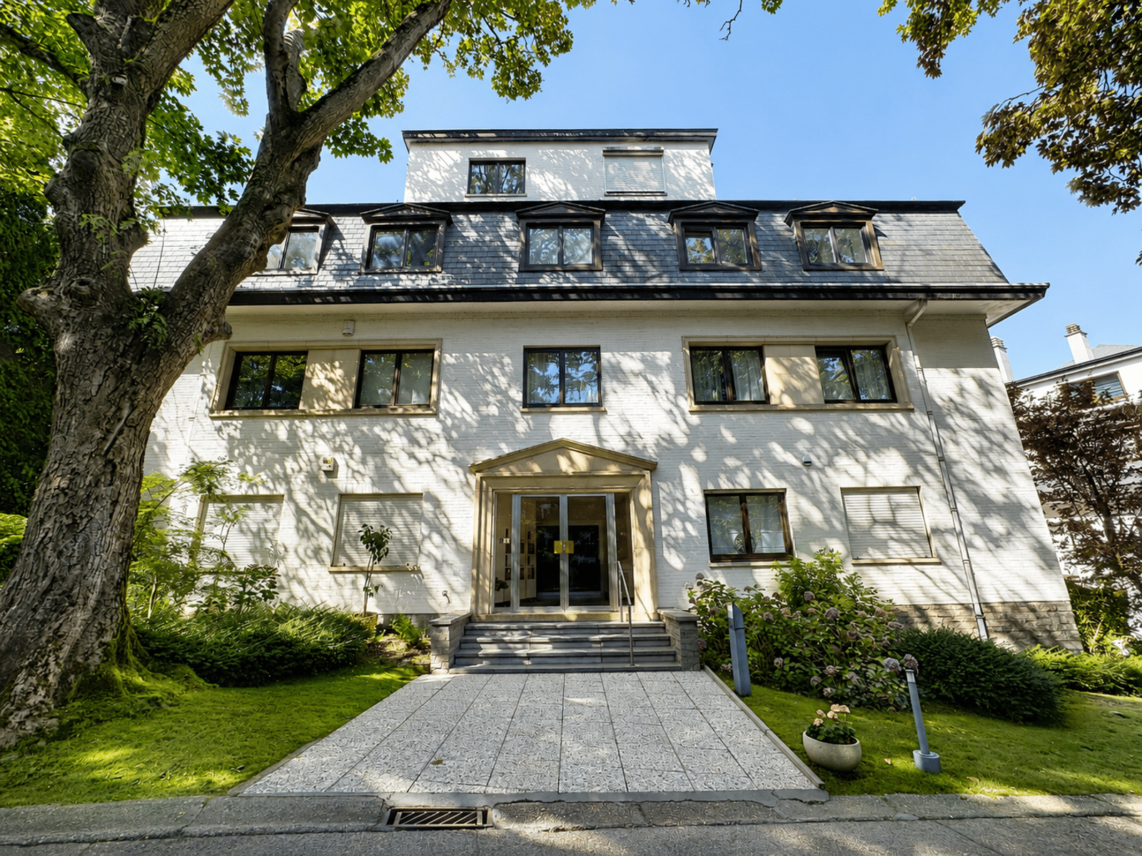 Façade de Maison Bourgeoise – You Real Estate Agency Façade élégante de maison bourgeoise avec jardin paysager et entrée centrale.