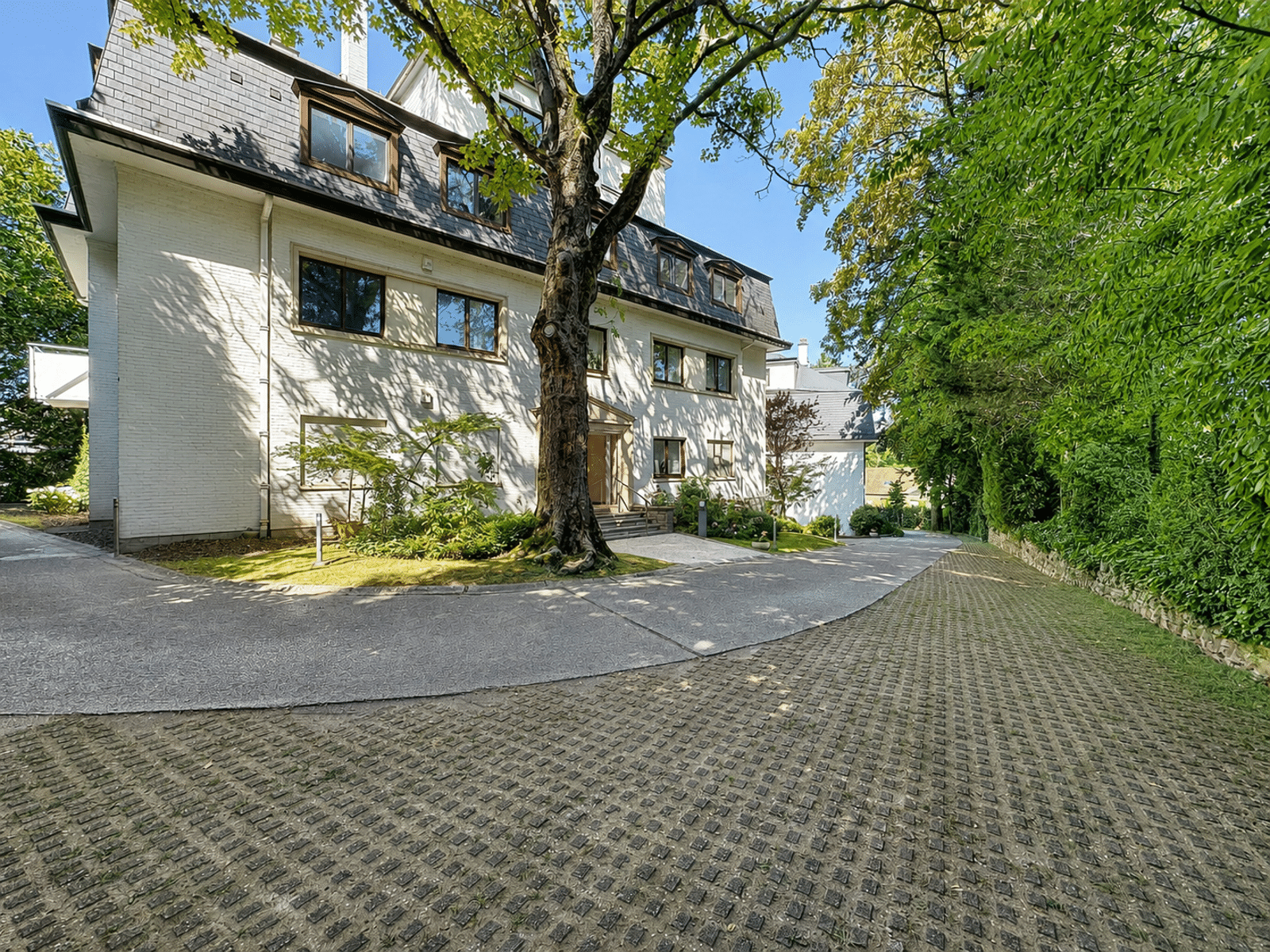 Maison de Prestige avec Jardin Arboré – You Real Estate Agency Maison de prestige avec façade blanche, jardin arboré et allée privée.
