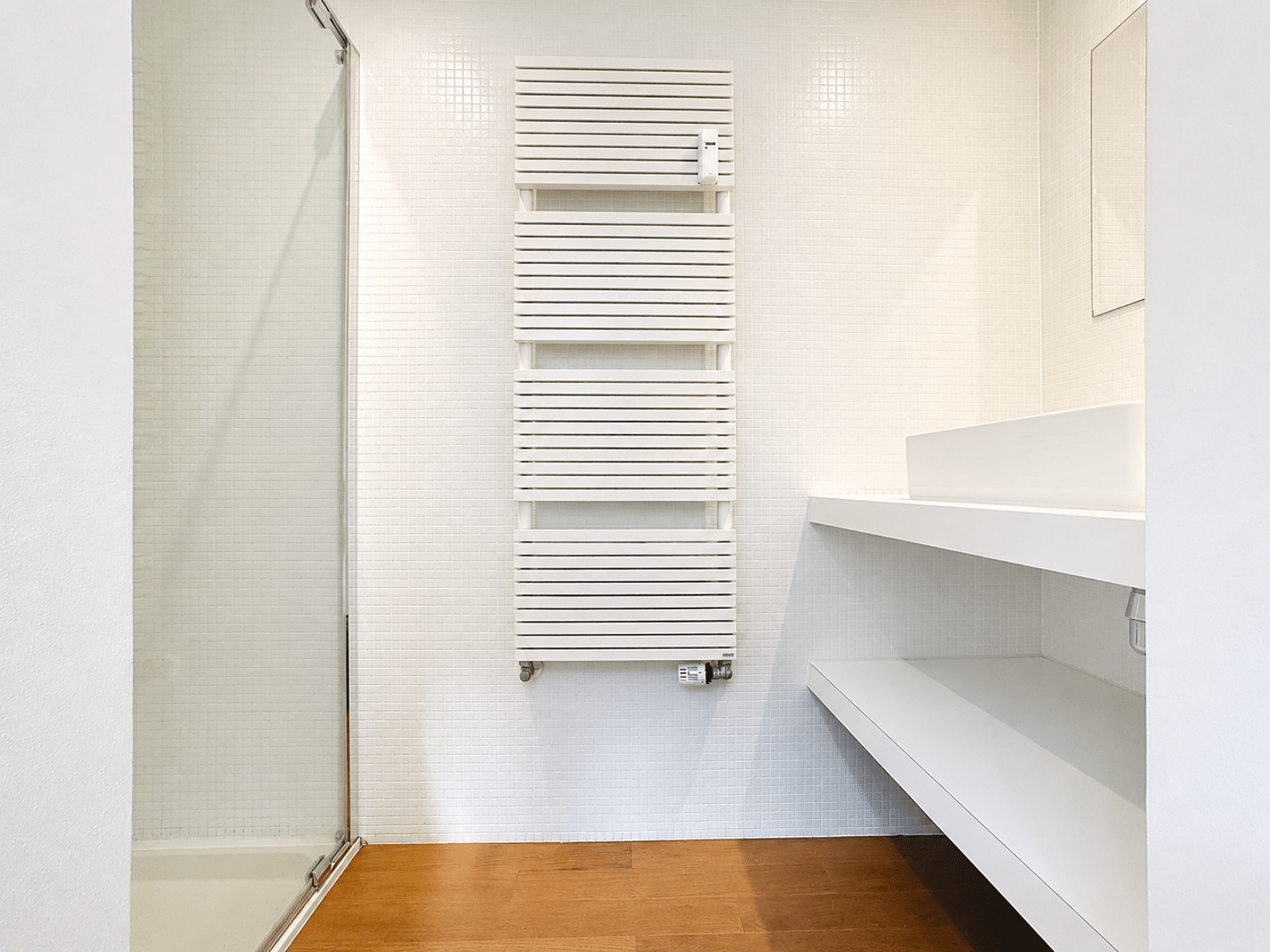 whise photo 13 White tiled bathroom with a vertical white radiator, glass shower on the left, and a white vanity on the right.