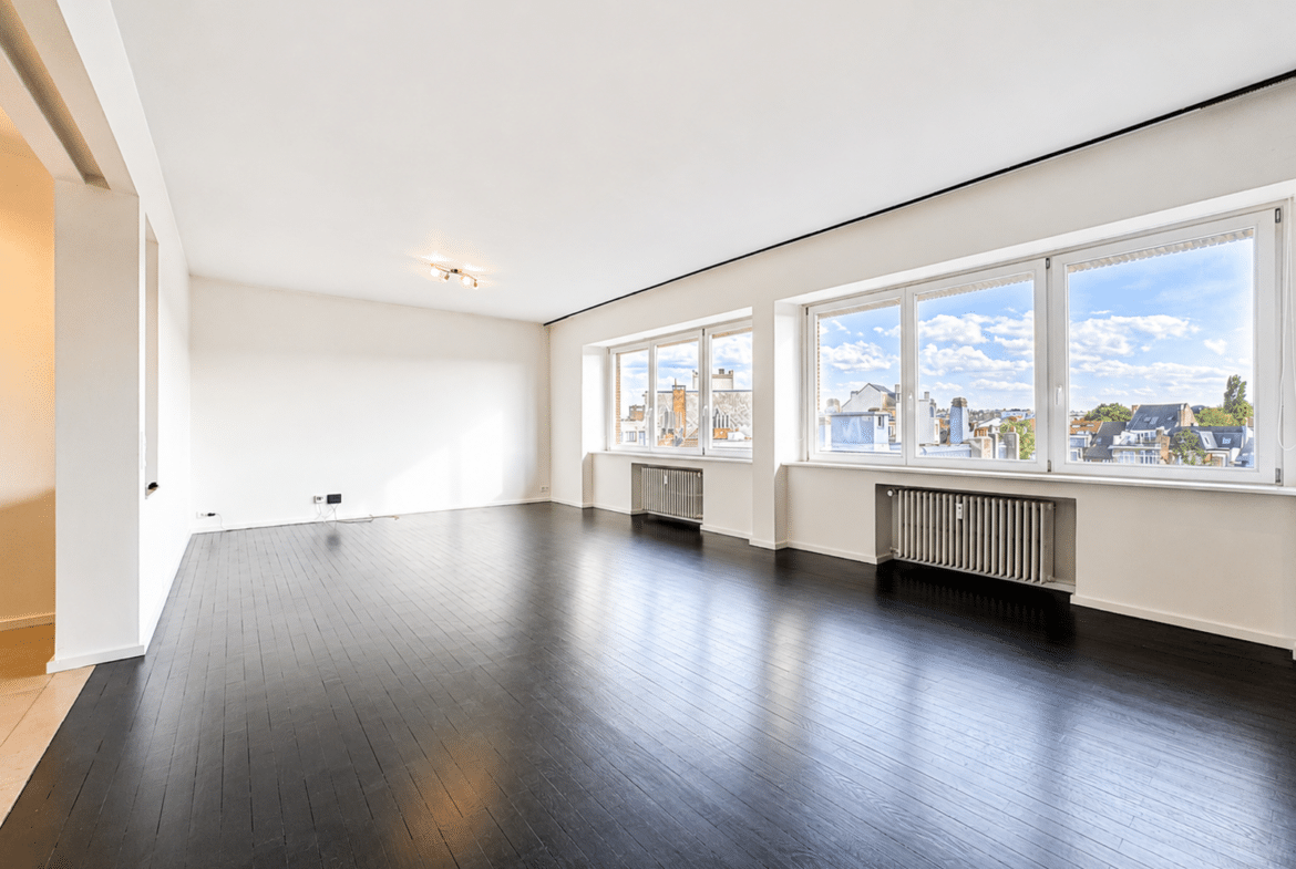 Bright living room in an unfurnished apartment with dark hardwood floors and large windows.