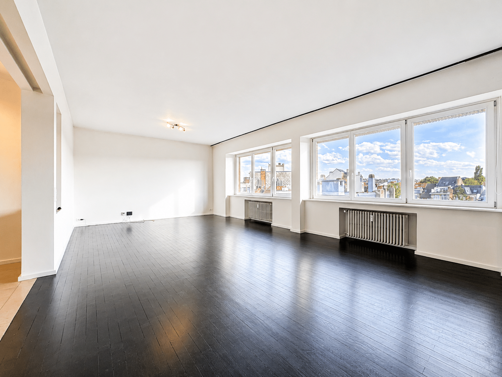 Salon Lumineux avec Parquet Foncé – You Real Estate Agency Salon lumineux d’appartement vide avec parquet foncé et grandes fenêtres.
