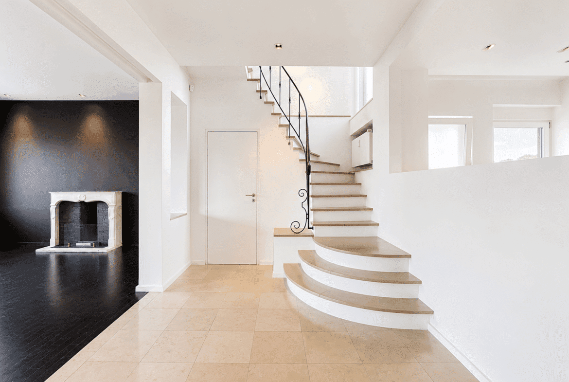 A bright entryway with a stylish staircase and a living room with a fireplace in a contemporary home.