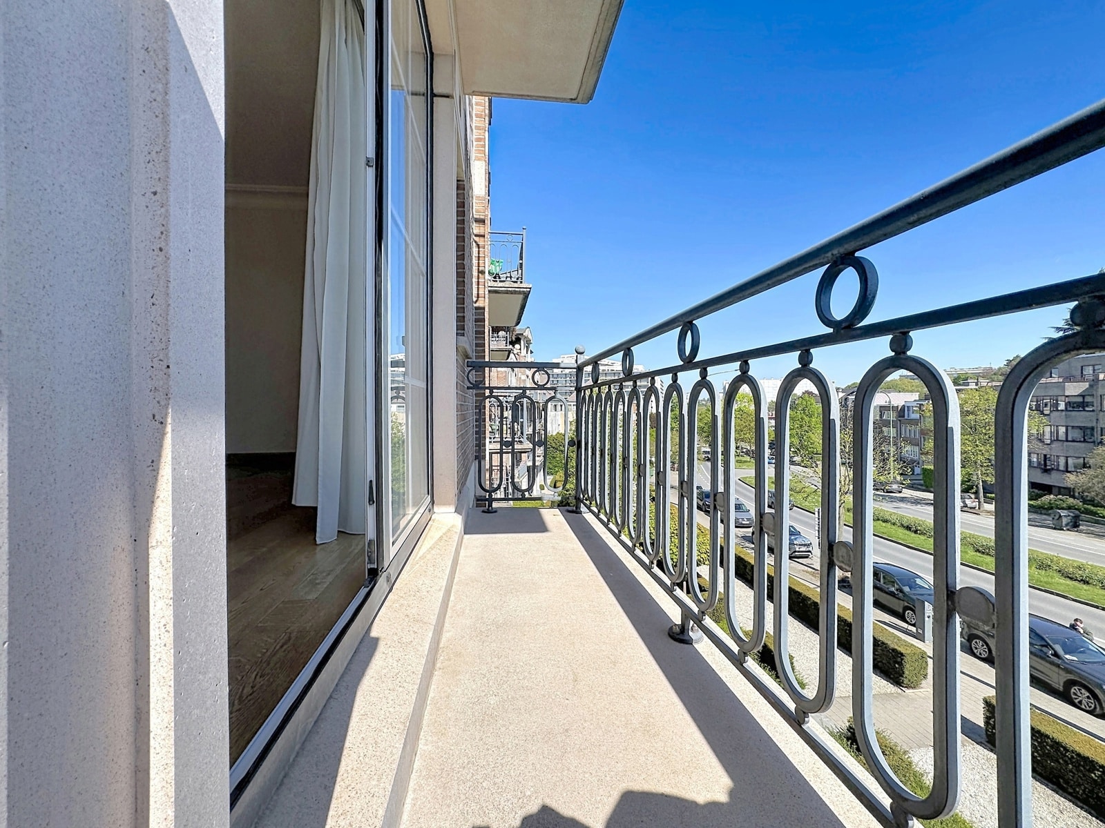 whise photo 8 Balcony with decorative iron railing overlooking a city street on a sunny day.