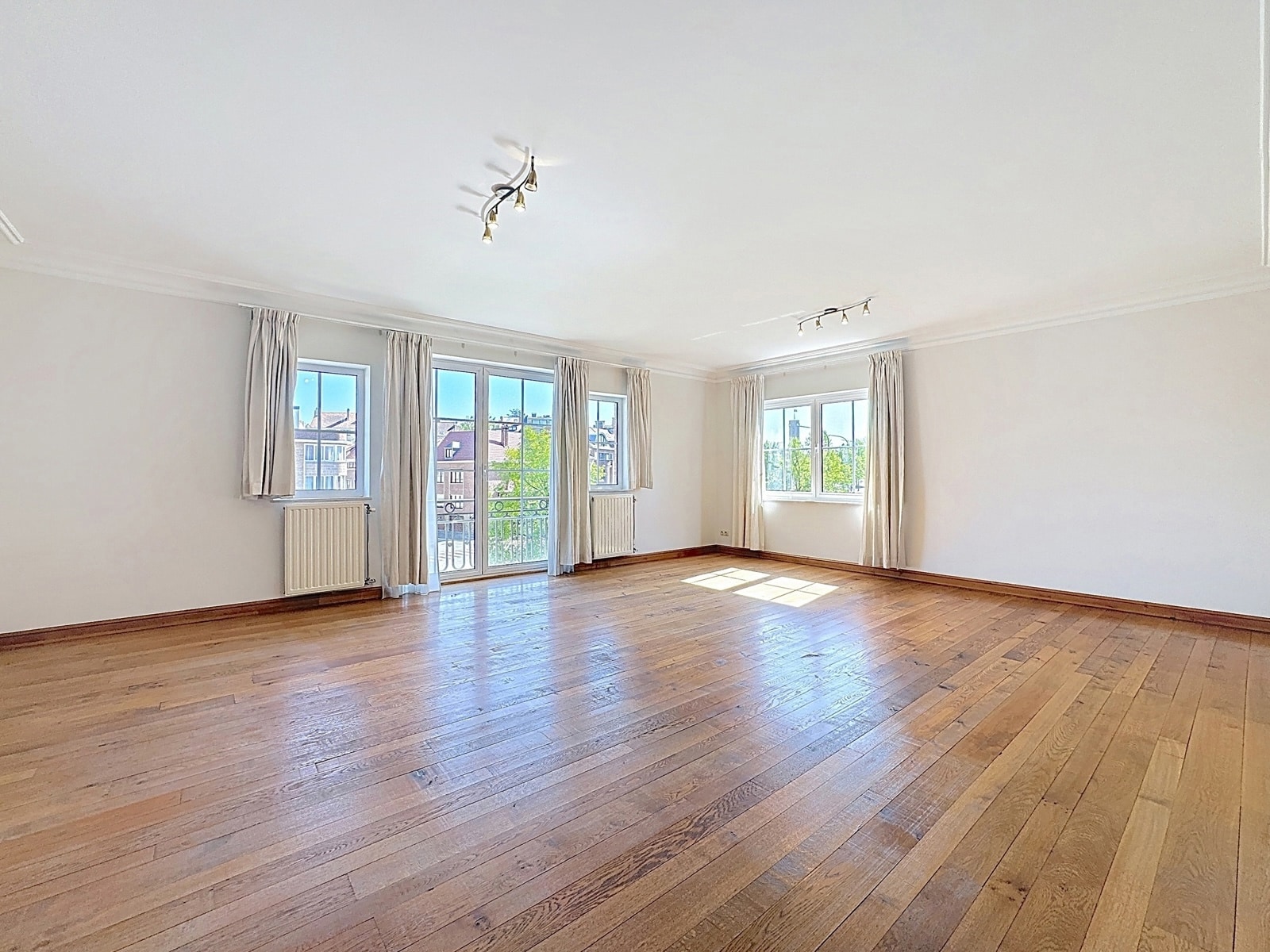 Salon Lumineux avec Parquet et Balcon – You Real Estate Agency Salon lumineux avec parquet, grandes fenêtres et balcon dans appartement spacieux.