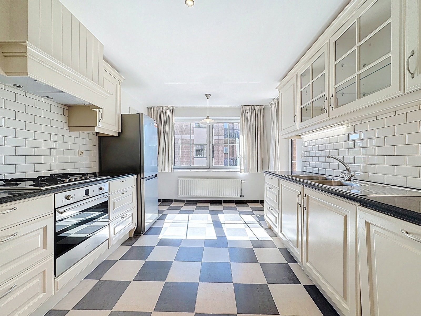 whise photo 2 Bright white kitchen with a blue-and-white checkerboard floor, white cabinets, stainless appliances, and a window at the far end letting in light.