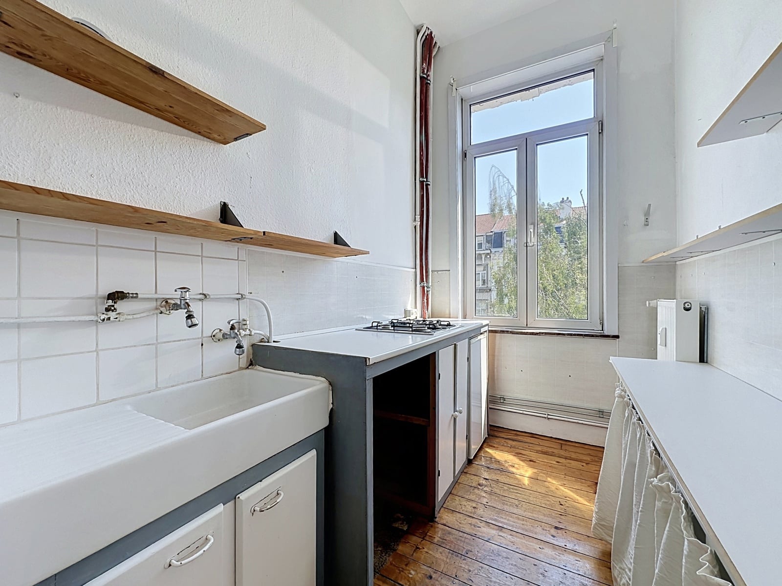 Cuisine en Longueur Lumineuse – You Real Estate Agency Cuisine d’appartement en longueur, lumineuse, avec étagères en bois et grande fenêtre.
