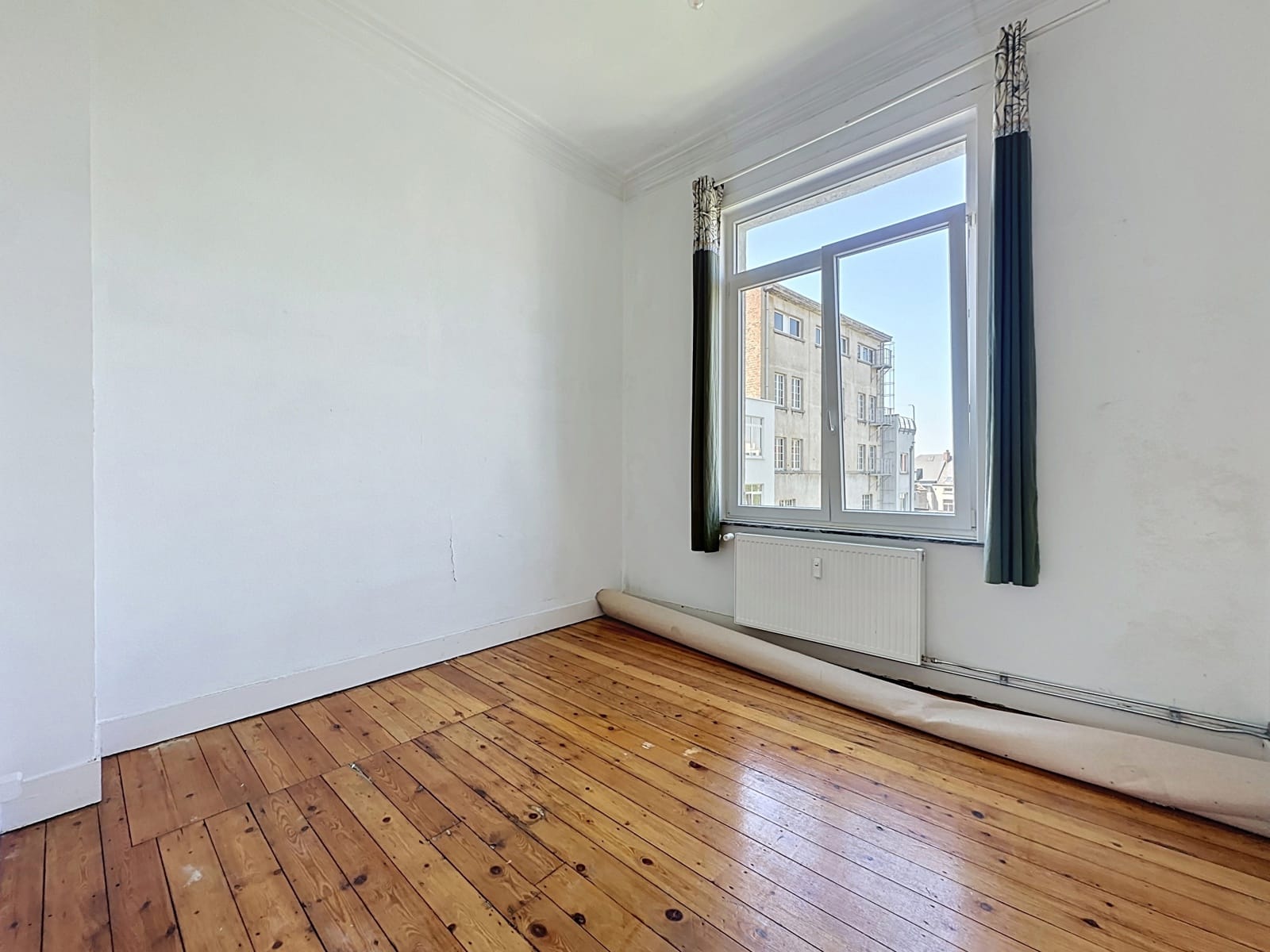 Pièce Vide Lumineuse avec Parquet – You Real Estate Agency Pièce vide d’appartement lumineux avec parquet, fenêtre ouverte et radiateur.