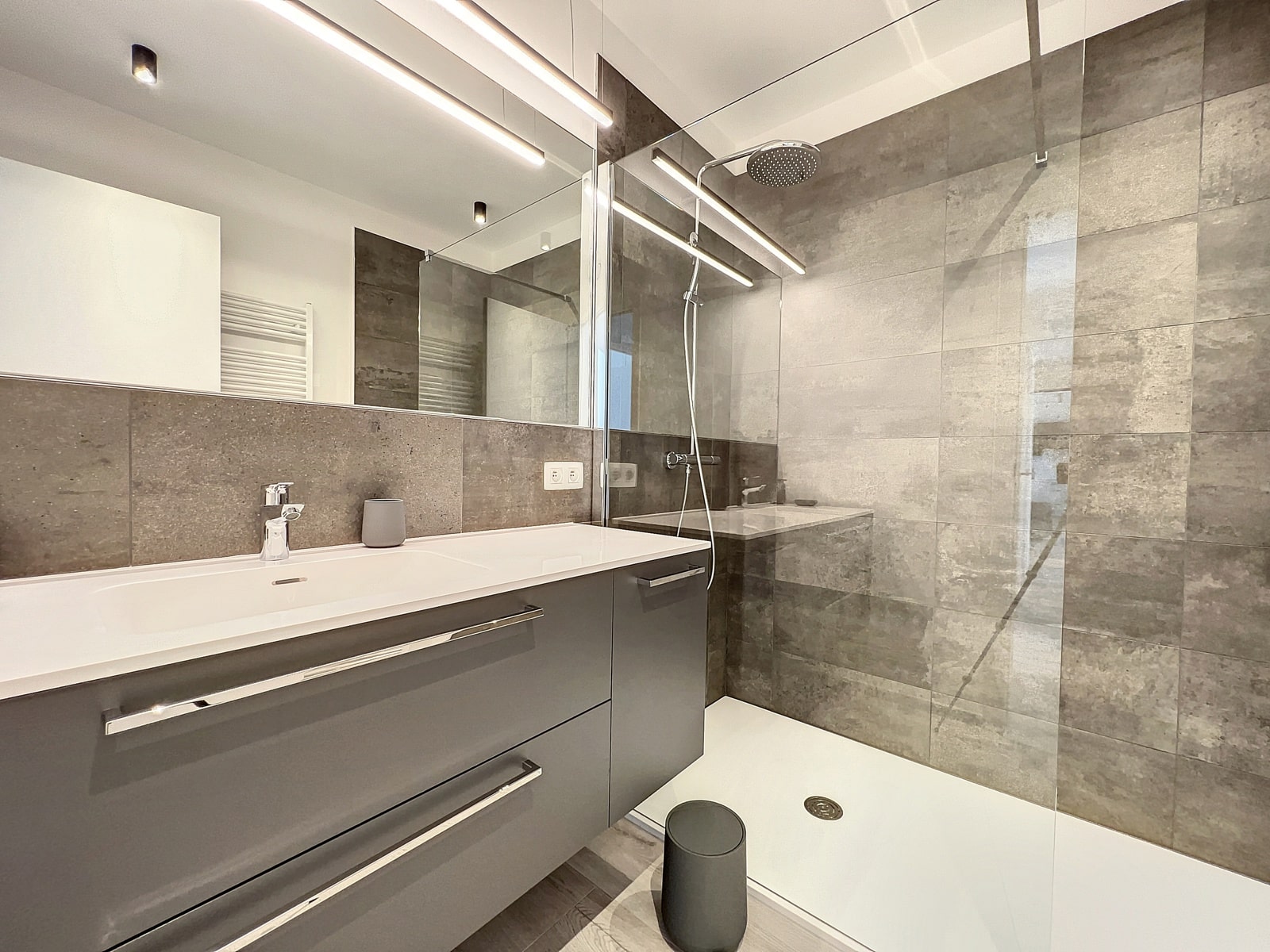 whise photo 7 Modern bathroom with a gray double vanity, white countertop, and large mirror reflecting a glass shower enclosure.