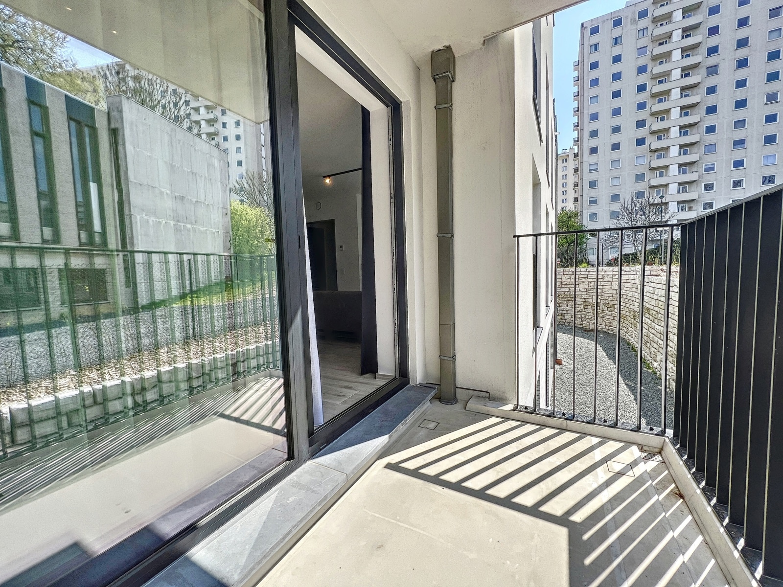 whise photo 5 Balcony with a metal railing outside a modern apartment; sliding glass door open to a living area, tall buildings in the background.