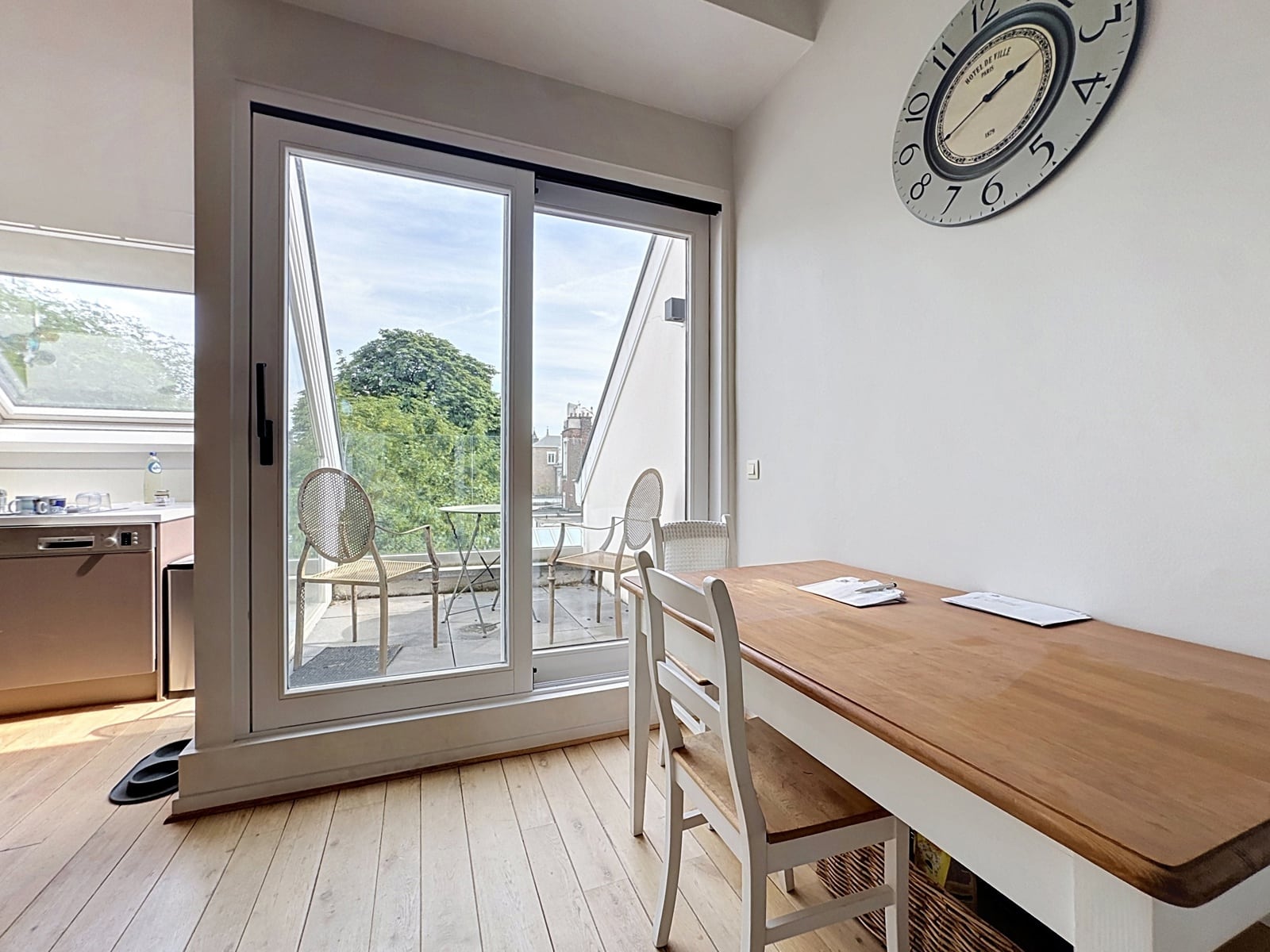 Coin Repas Lumineux avec Balcon – You Real Estate Agency Coin repas lumineux d’appartement avec balcon terrasse, cuisine ouverte et vue arborée.