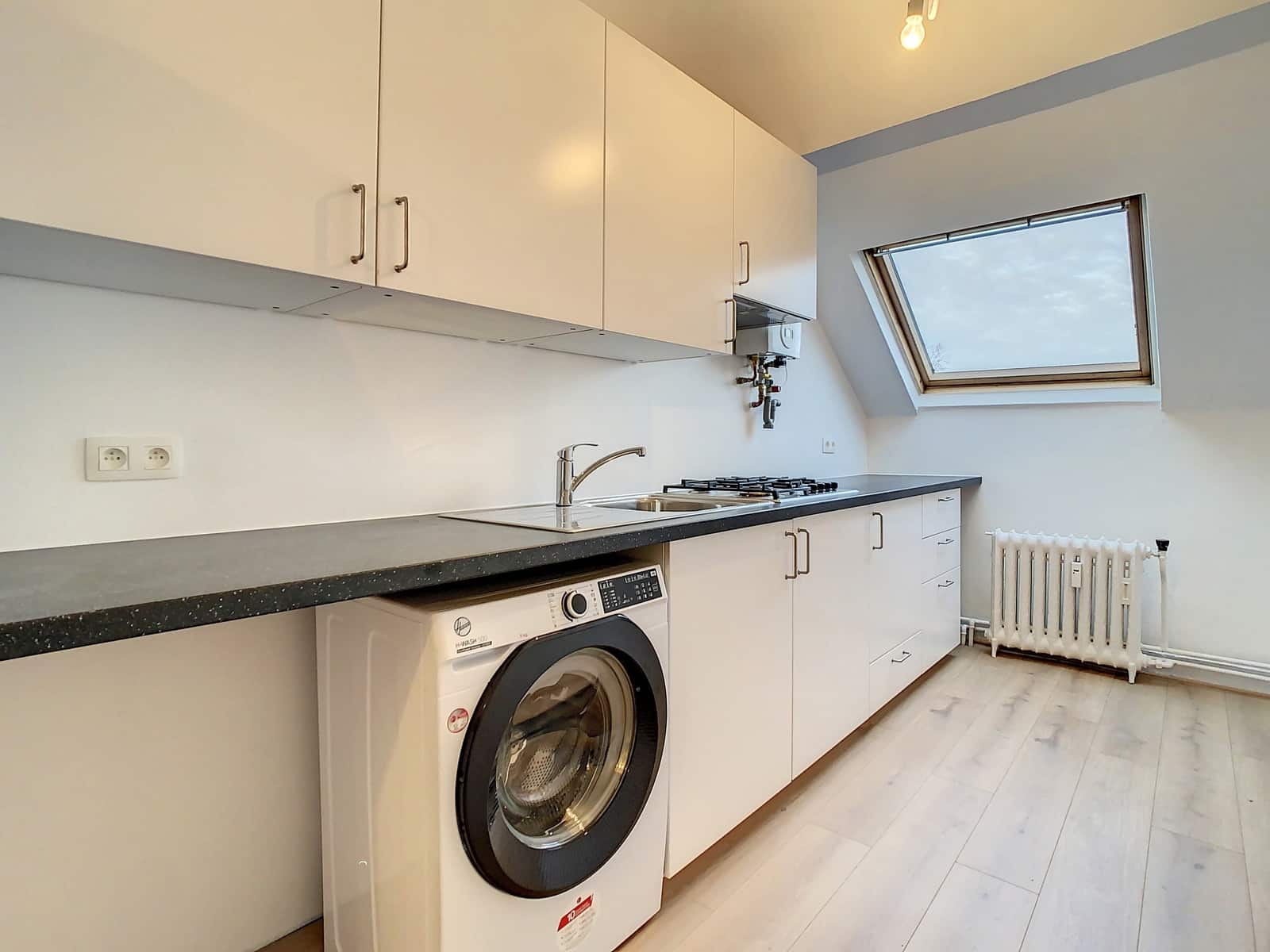 Cuisine Moderne Sous Combles – You Real Estate Agency Cuisine moderne d’appartement sous combles avec rangements blancs et puits de lumière.