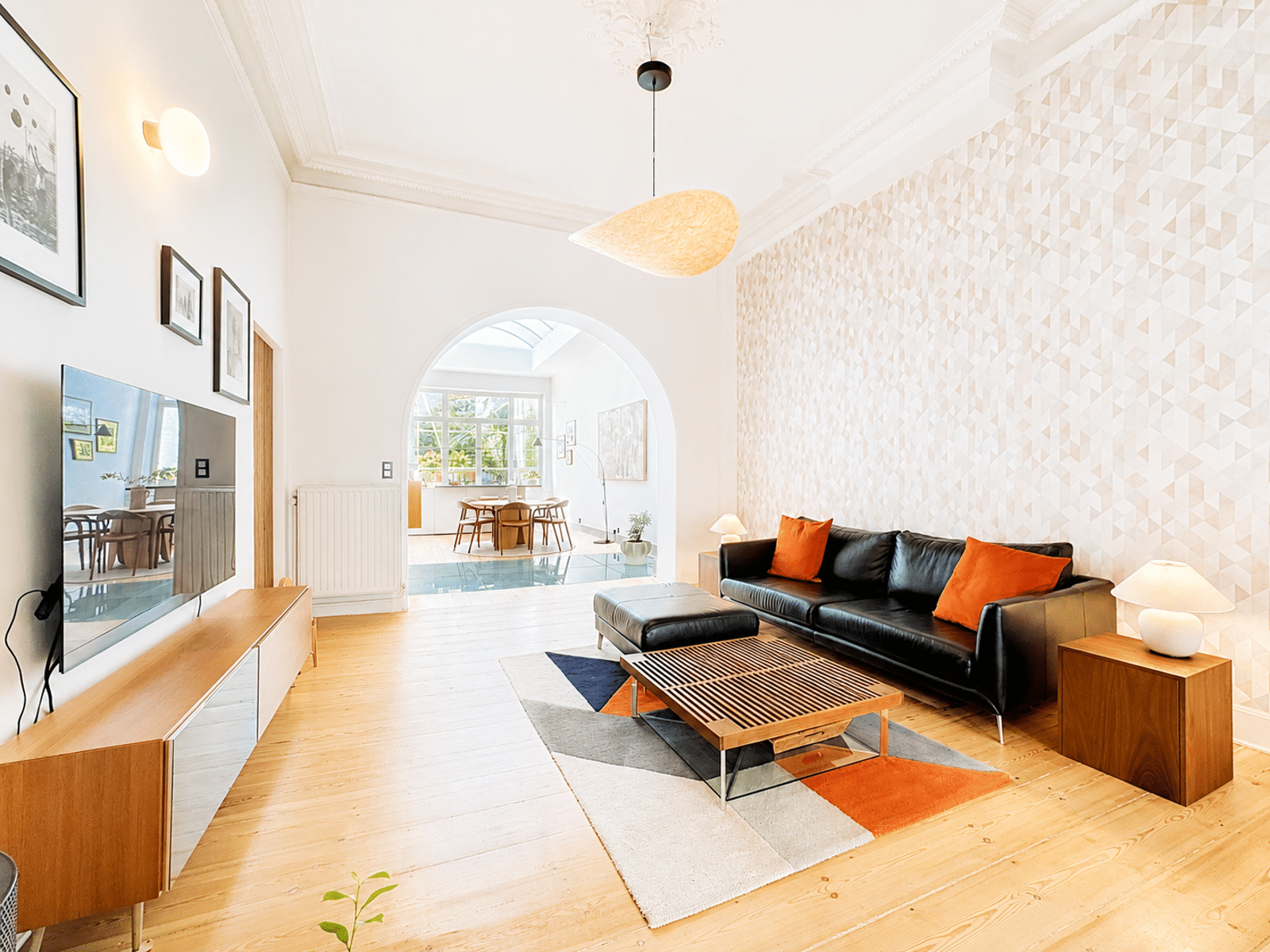 Salon Élégant avec Hauts Plafonds – You Real Estate Agency Salon élégant d’appartement avec canapé noir, hauts plafonds moulurés et coin salle à manger lumineux.