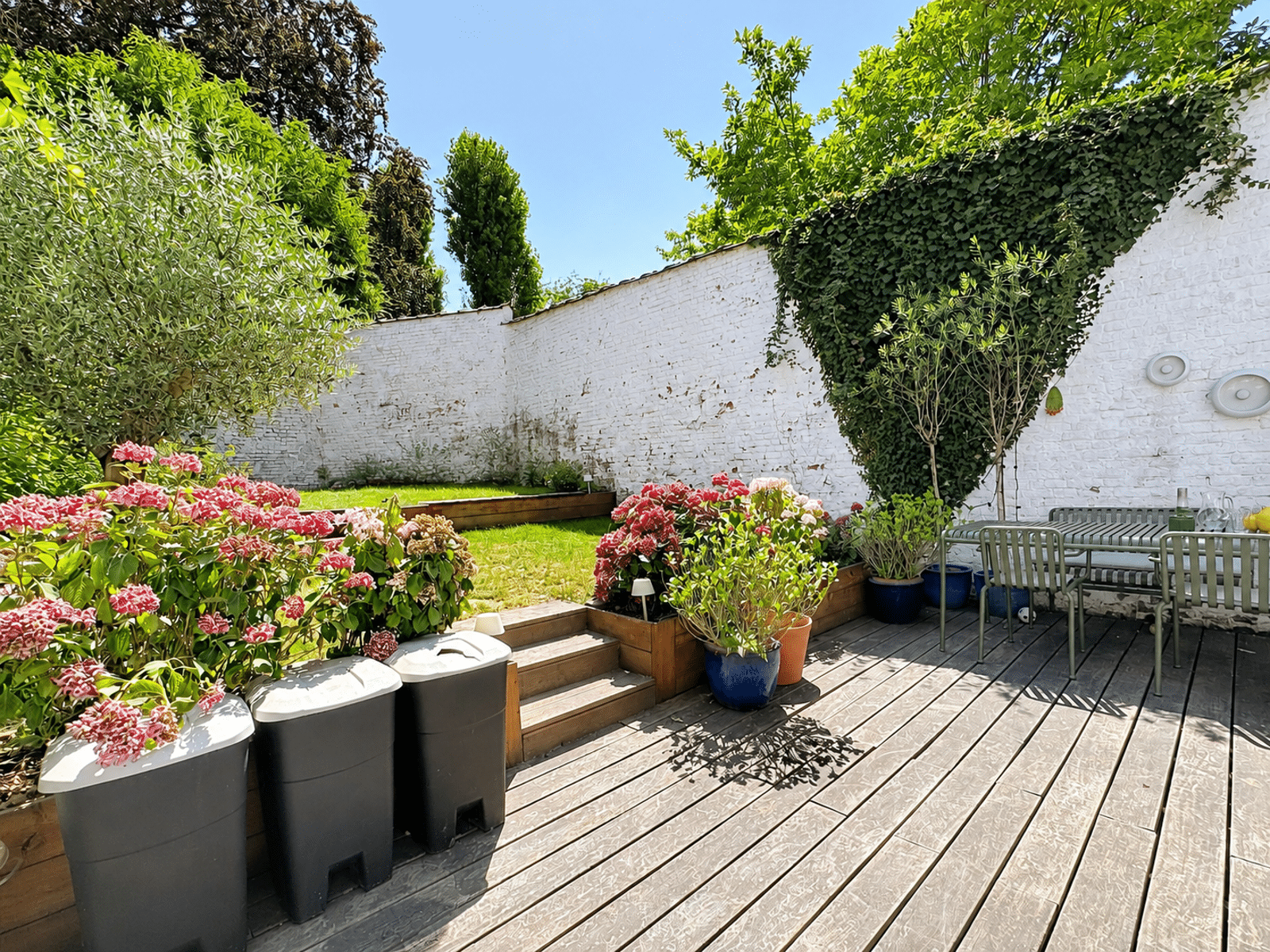 Jardin Paysager et Terrasse en Bois – You Real Estate Agency Terrasse en bois avec jardin paysager et coin repas d’une maison.