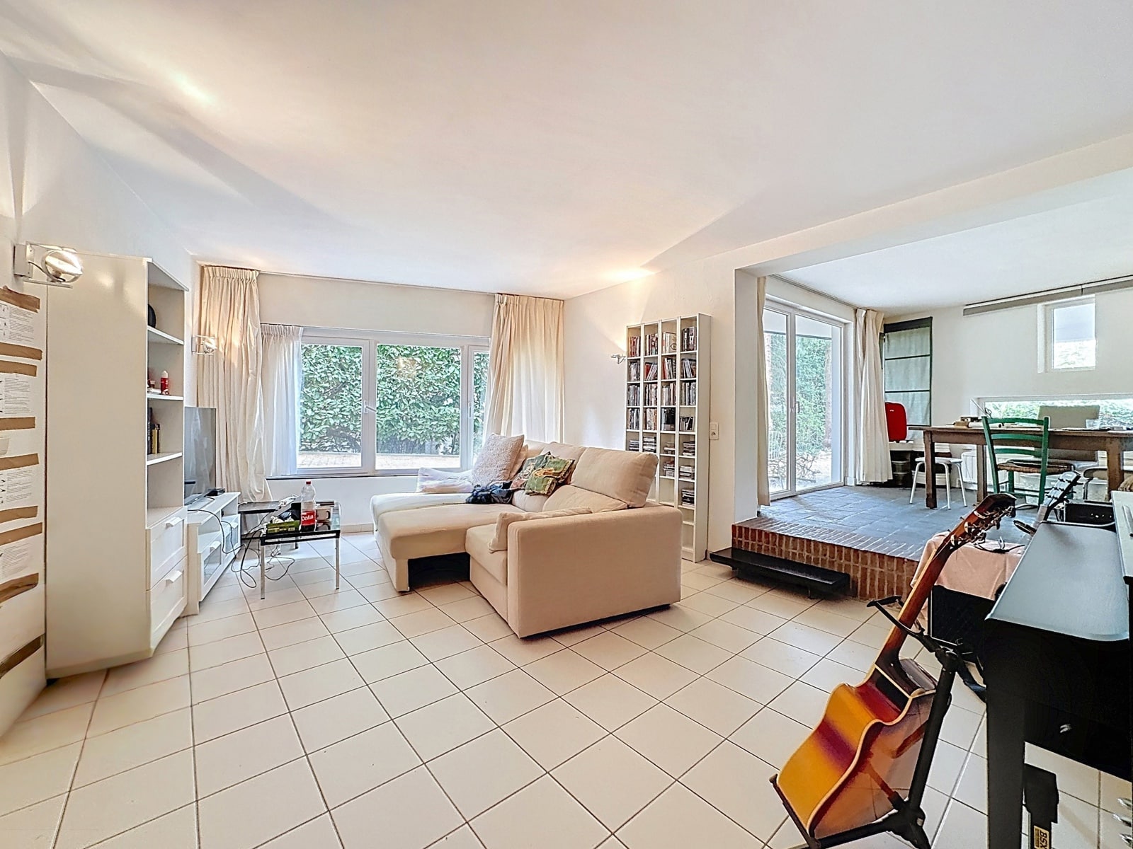 Bright living room with dining room - You Real Estate Agency Bright living room in an apartment with a raised dining area and large floor-to-ceiling windows.