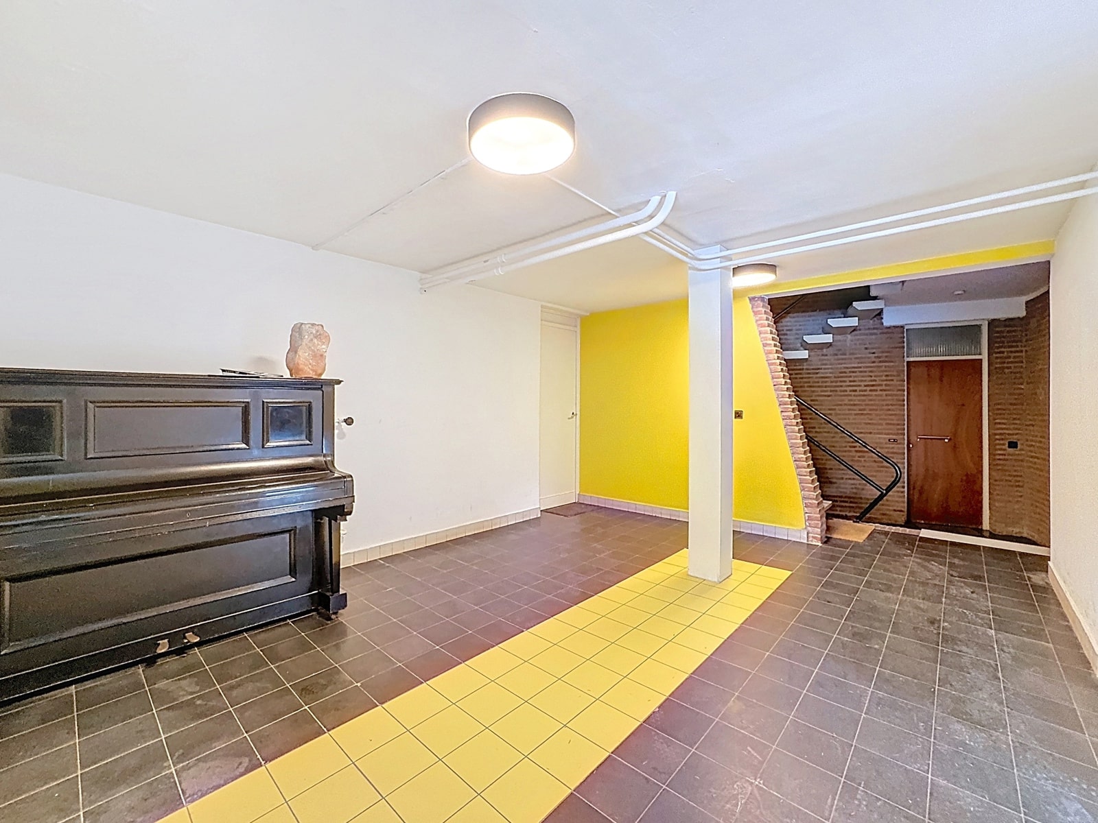 Multipurpose Room with Piano – You Real Estate Agency A multipurpose room with a piano, a yellow wall, and a staircase in a renovated apartment.