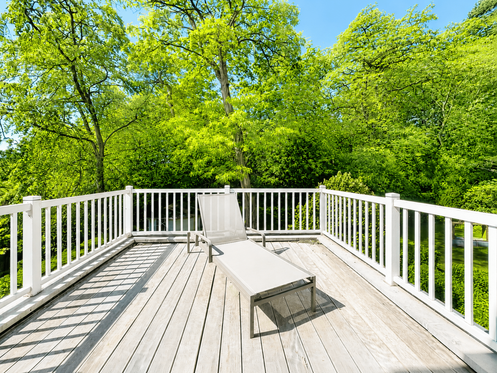 Terrasse Ensoleillée Avec Transat – You Real Estate Agency Terrasse en bois ensoleillée avec transat, entourée d’arbres verdoyants.