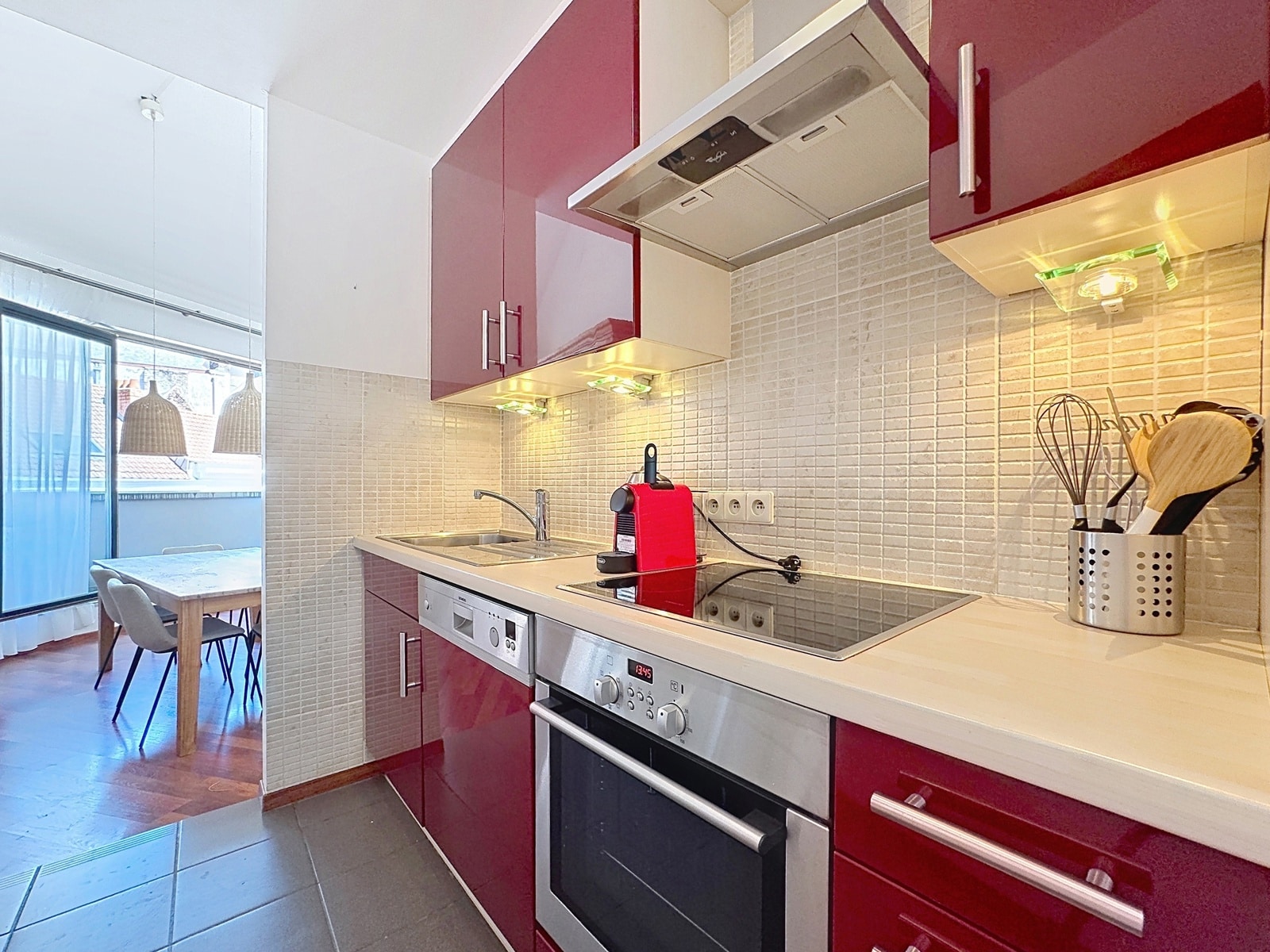 Cuisine Moderne avec Coin Repas – You Real Estate Agency Cuisine équipée moderne avec meubles bordeaux et coin repas lumineux en appartement.