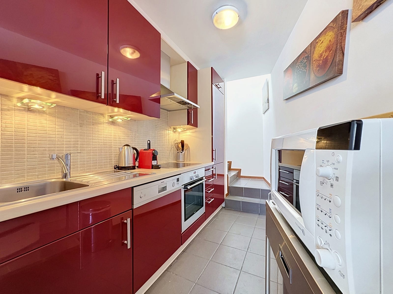 Cuisine Équipée Rouge Brillante – You Real Estate Agency Cuisine équipée moderne aux meubles rouges brillants dans un appartement.
