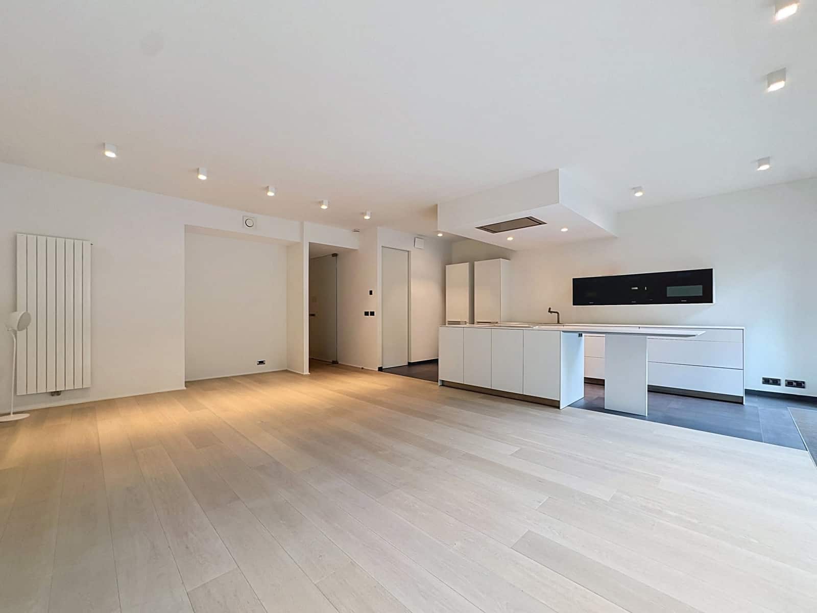 Séjour Ouvert avec Cuisine Moderne – You Real Estate Agency Appartement moderne avec salon ouvert, cuisine équipée blanche et parquet clair.
