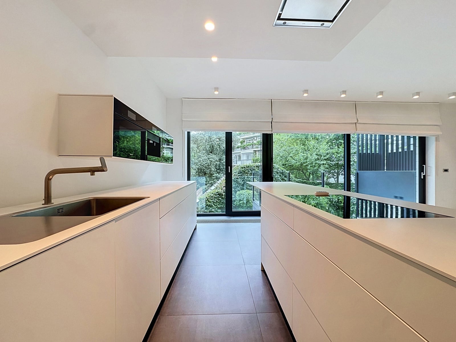 whise photo 6 Modern white kitchen with a long island, stainless sink, and brass faucet facing a garden view.