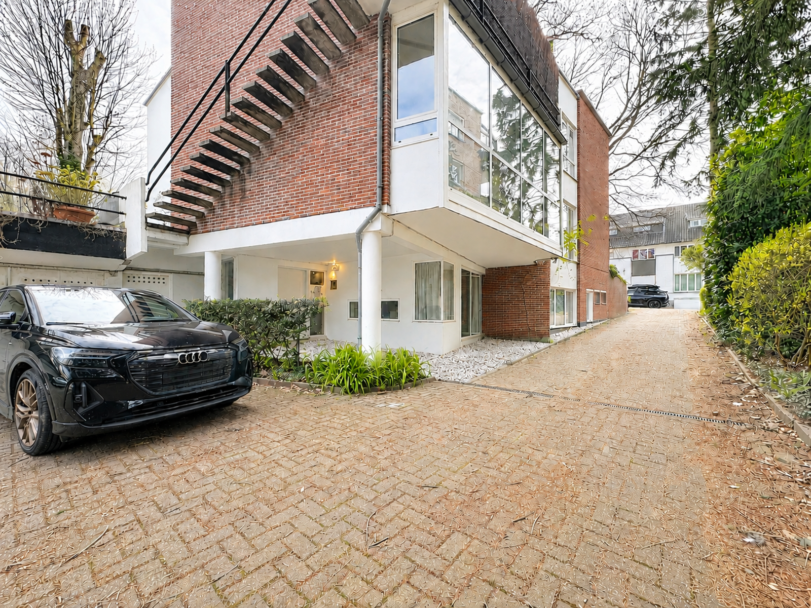whise photo 13 A modern brick building with a large glass-enclosed upper level, white columns, and a black Audi SUV parked on a brick driveway.