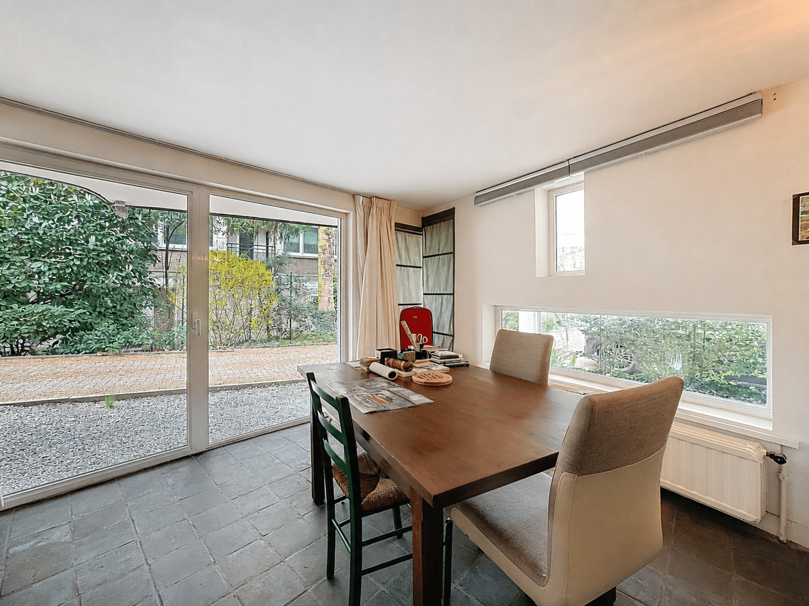 whise photo 4 A bright dining room with a wooden table and four chairs, featuring large glass doors that open onto the garden outside.