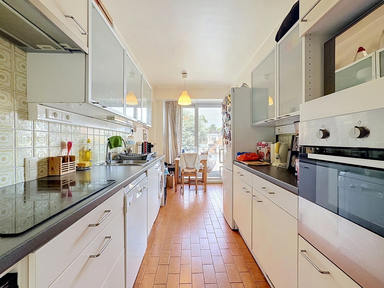 Cuisine Équipée Lumineuse en Couloir – You Real Estate Agency Cuisine équipée lumineuse en couloir avec coin repas dans appartement.