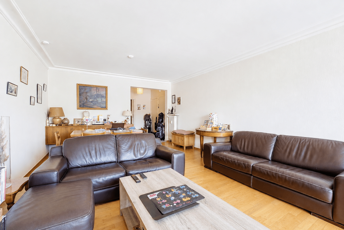 Salon spacieux et lumineux avec parquet, canapés en cuir et coin salle à manger.