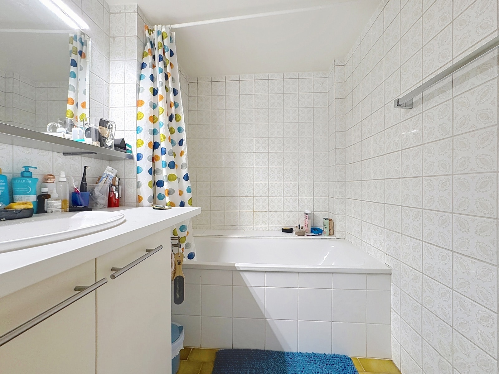 whise photo 11 Bright bathroom with white tiled walls, a vanity with toiletries, and a colorful polka-dot shower curtain.