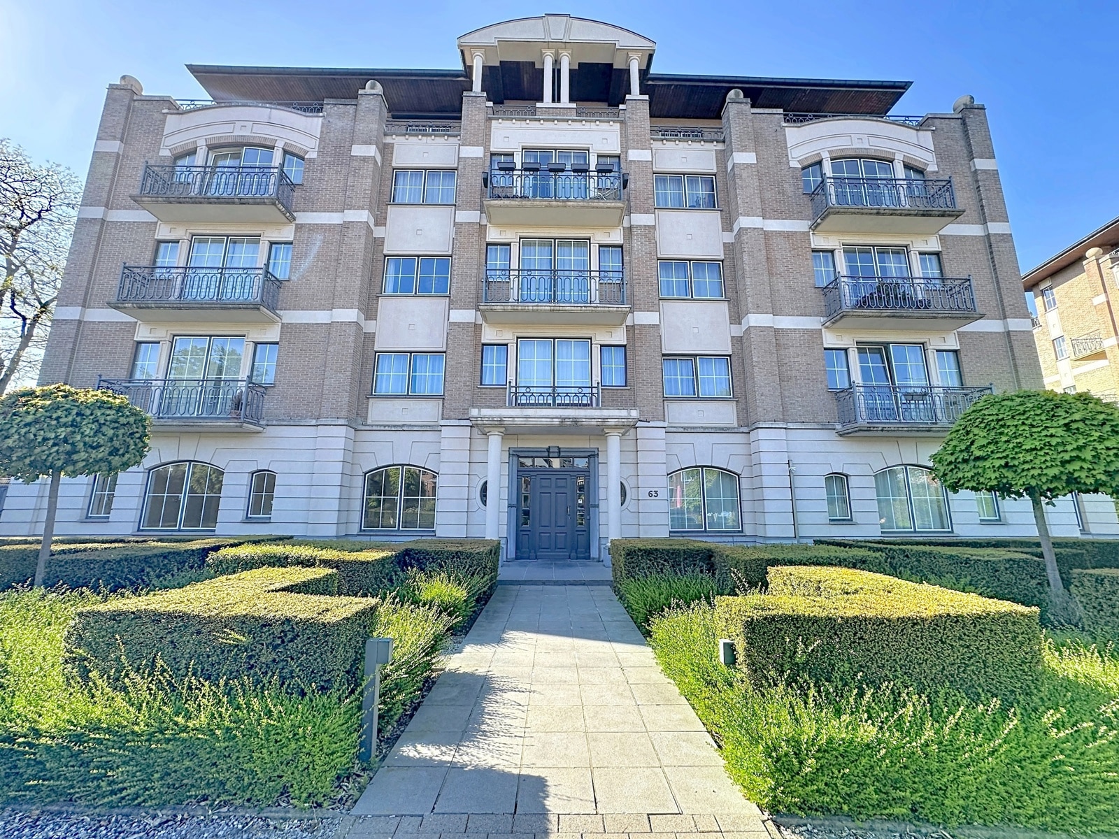Façade d’Immeuble avec Jardin – You Real Estate Agency Façade élégante d’immeuble à appartements avec entrée prestigieuse, balcons et jardin soigné.