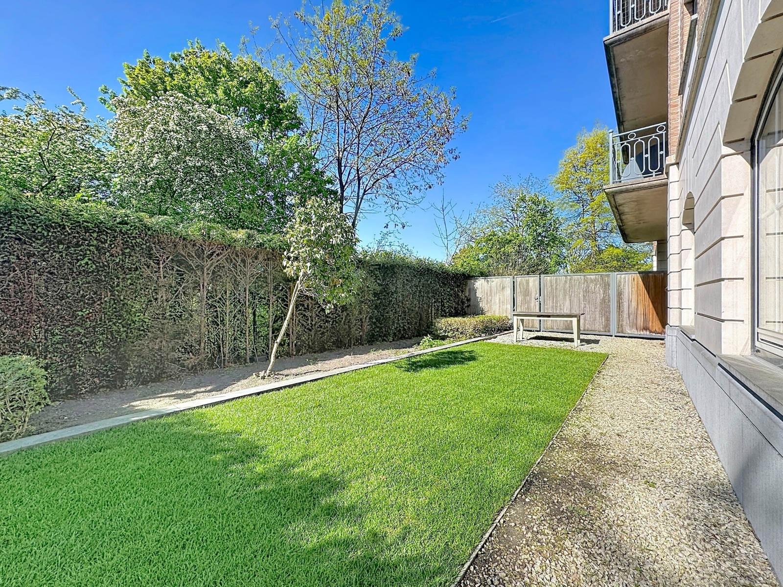 Jardin Privatif Ensoleillé – You Real Estate Agency Jardin privatif d’appartement avec pelouse, haies et balcons ensoleillés.