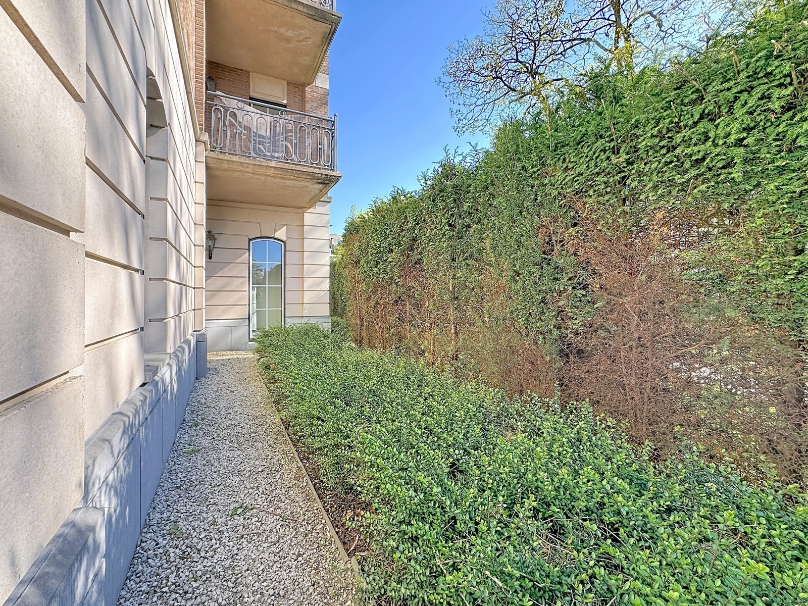 Façade Avec Allée Gravillonnée – You Real Estate Agency Maison élégante avec allée gravillonnée, balcon et haies dans jardin privé.