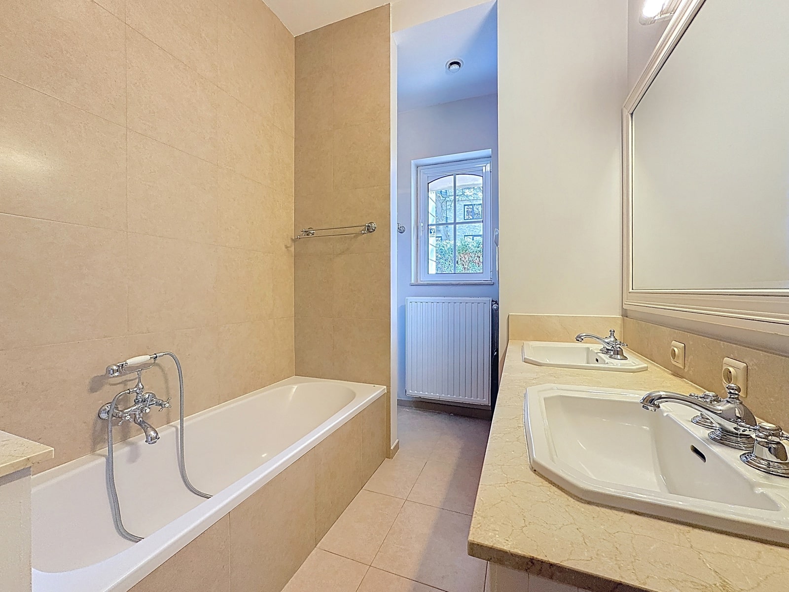Salle de Bain avec Double Vasque – You Real Estate Agency Salle de bain élégante avec baignoire, double vasque et fenêtre lumineuse.