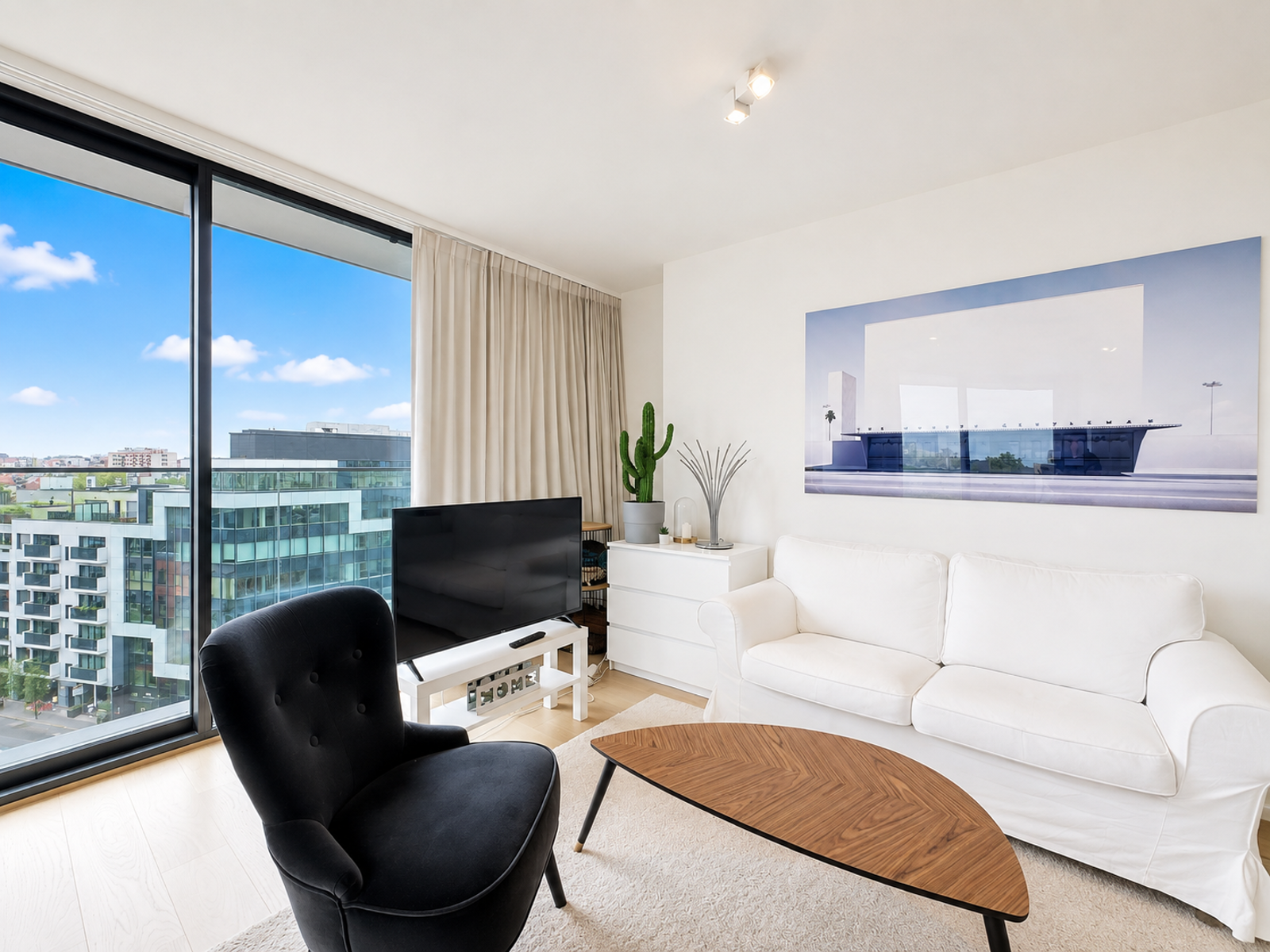 Salon Lumineux avec Vue Urbaine – You Real Estate Agency Salon lumineux d’appartement moderne avec vue urbaine et décoration minimaliste.
