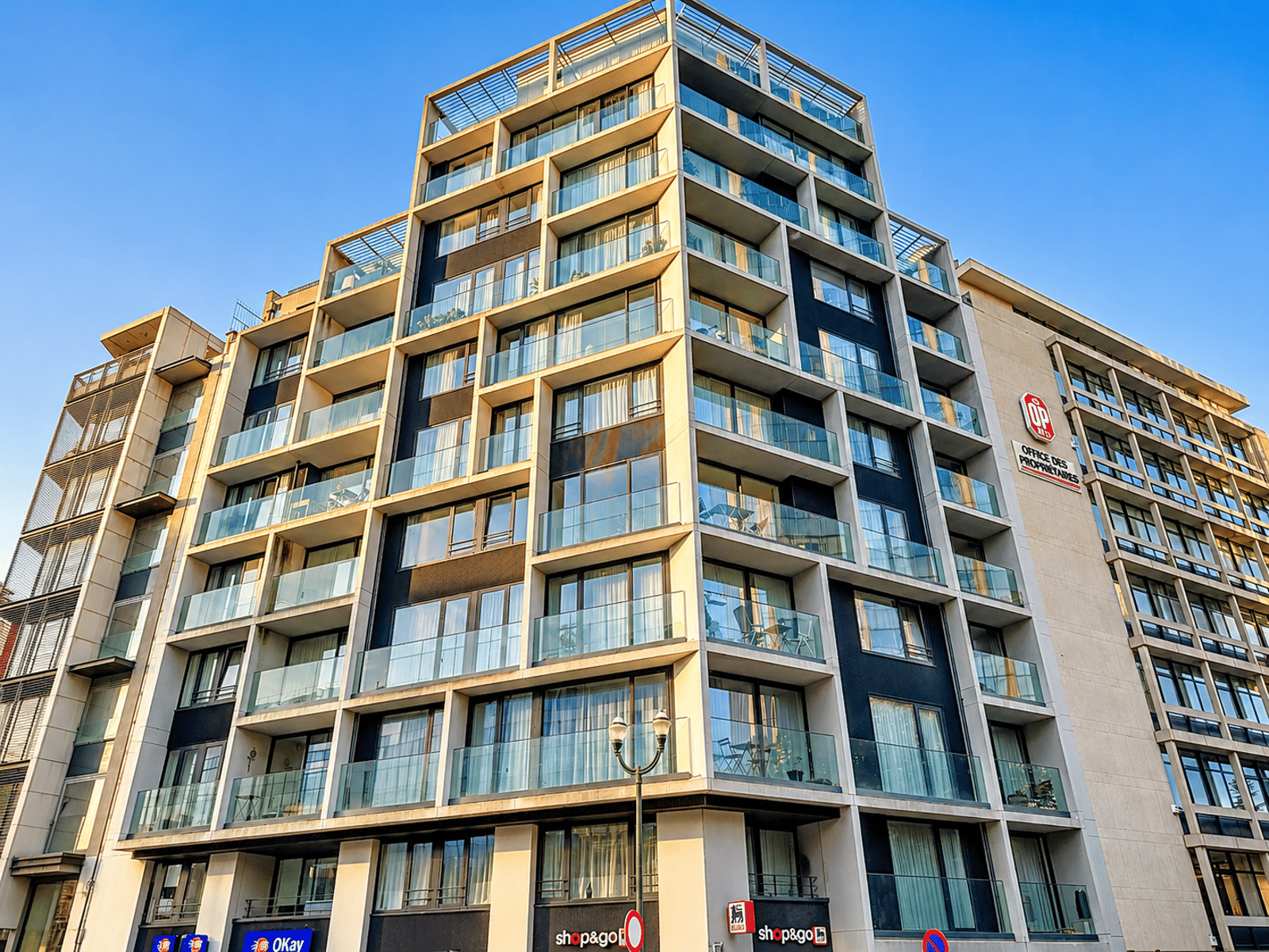 Immeuble Moderne Avec Balcons Vitrés – You Real Estate Agency Immeuble d’appartements moderne avec terrasses vitrées et commerces en rez-de-chaussée.
