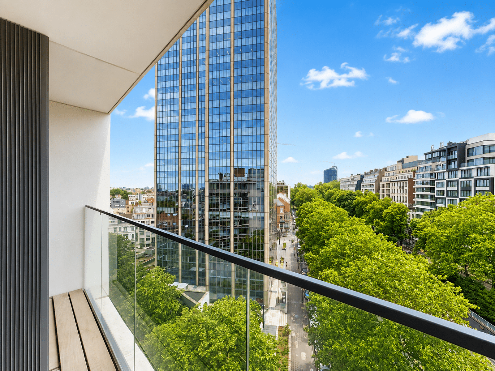 whise photo 14 Balcony with glass railing overlooking a tree-lined street and a tall glass skyscraper against a blue sky