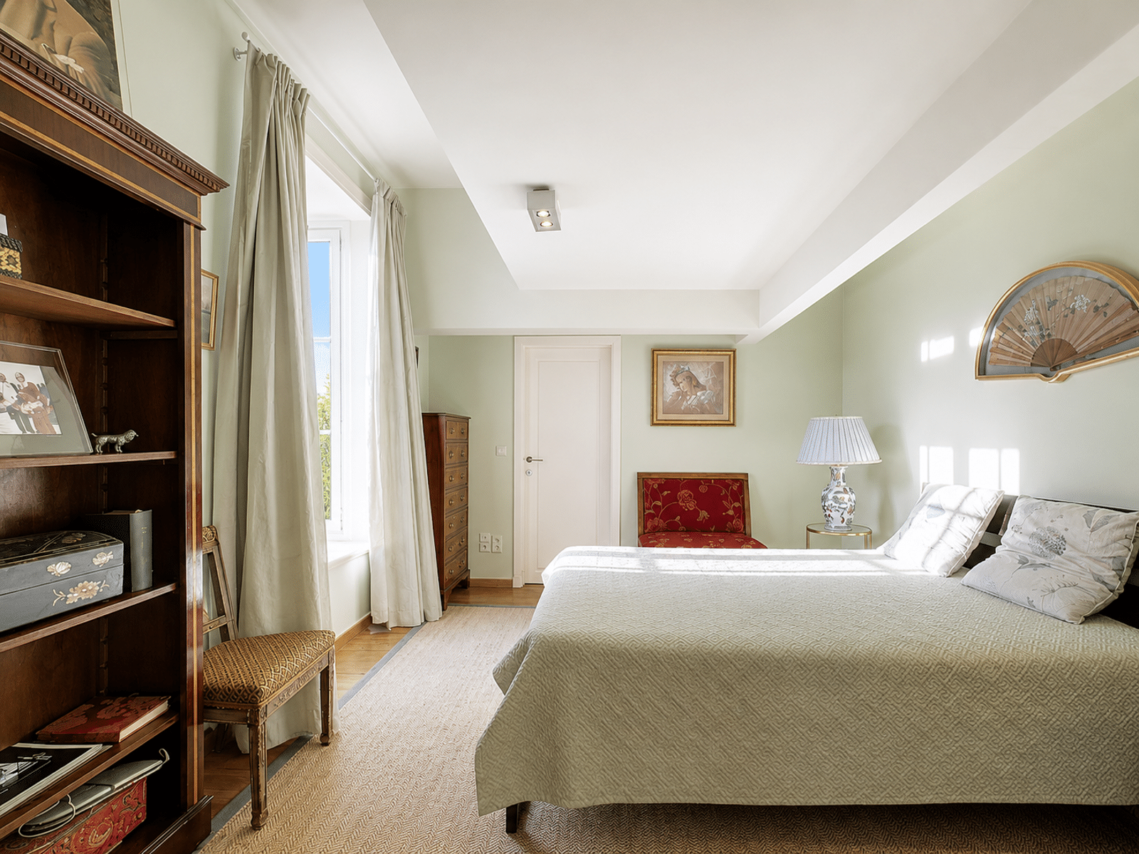 Bright and Elegant Room – You Real Estate Agency A bright bedroom in a house with a bed, antique furniture, and a large window.