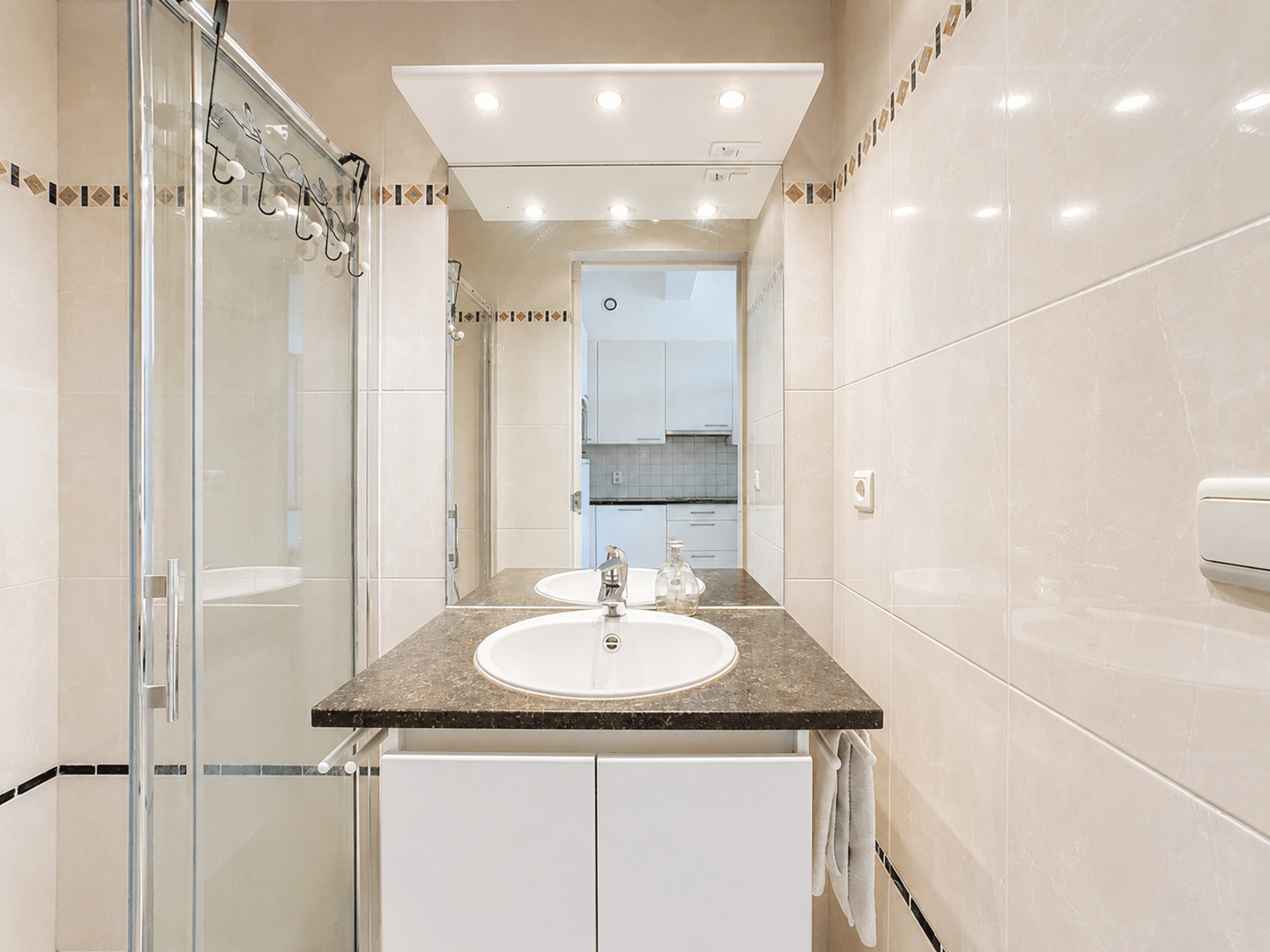 Bathroom with glass shower - You Real Estate Agency Modern apartment bathroom with a glass-enclosed shower, vanity, and large mirror.