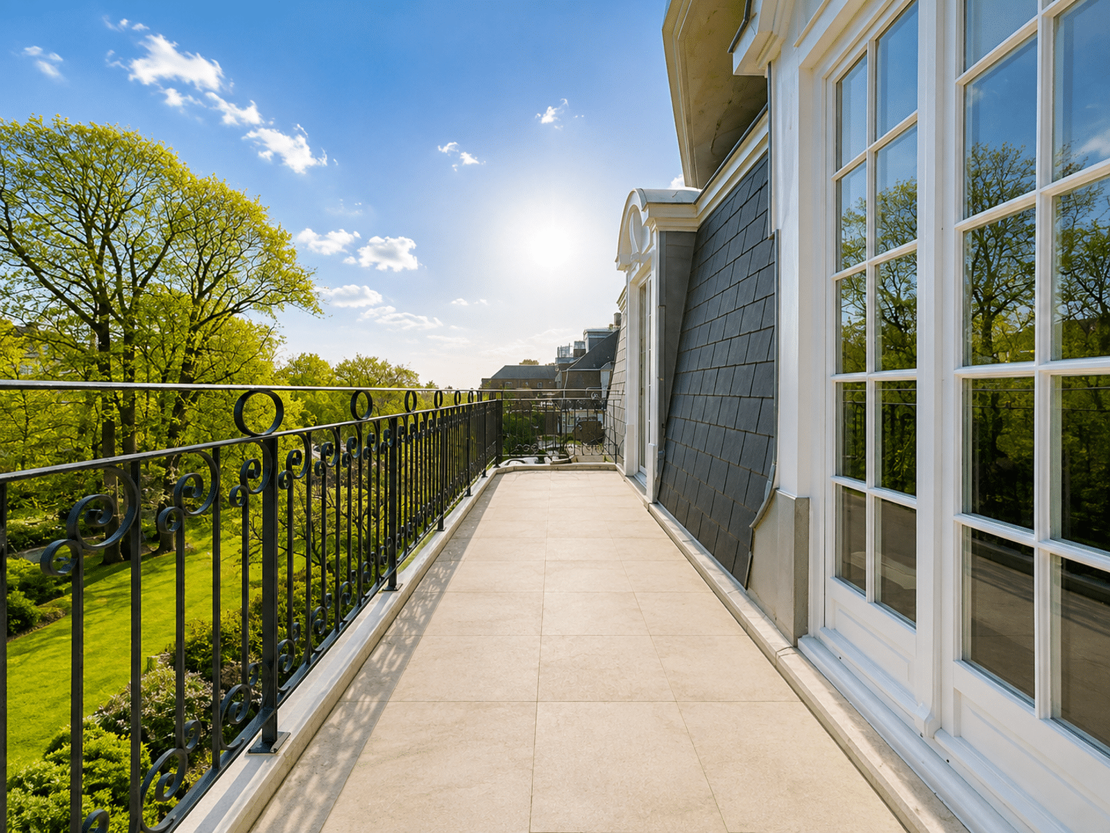 whise photo 16 A balcony with an ornate black railing overlooking green trees and a bright blue sky, with tall windows reflecting the outdoors.