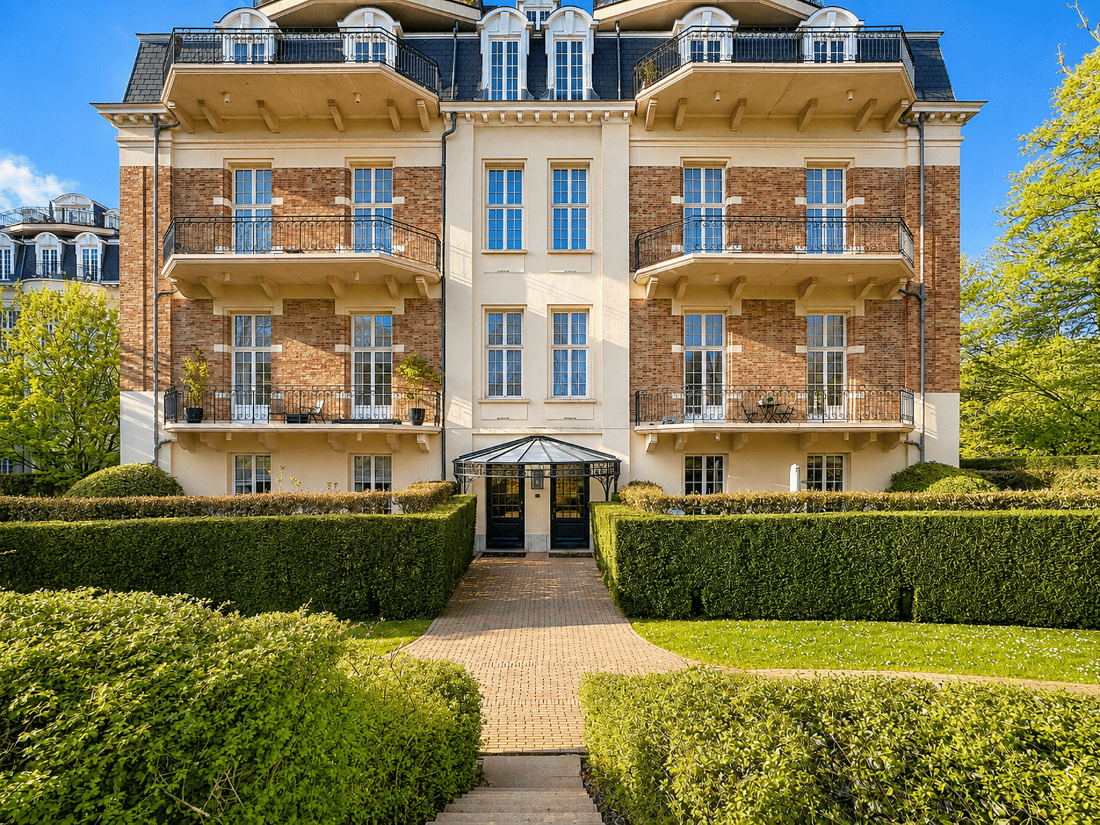 Elegant residential facade - You Real Estate Agency A luxury brick residence featuring apartments, balconies, and a landscaped garden.
