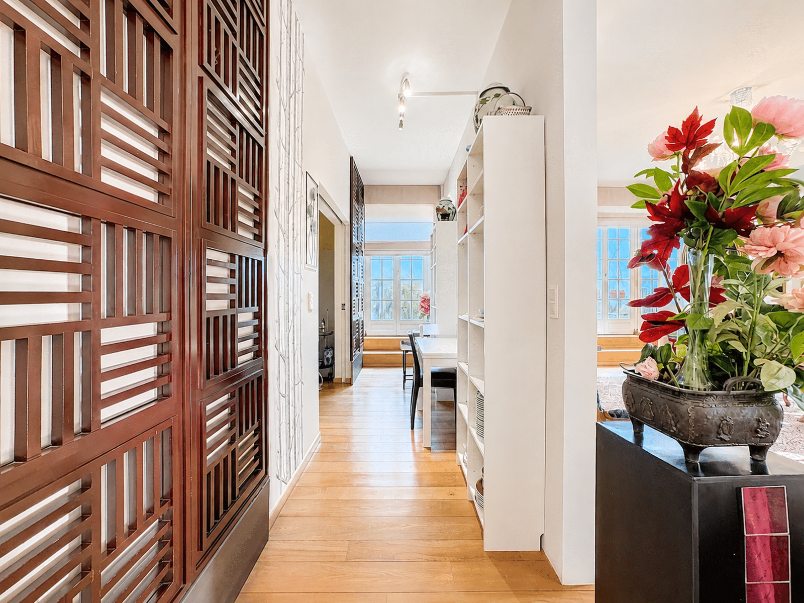Bright Hallway with Wooden Screen – You Real Estate Agency A bright apartment hallway with hardwood floors, decorative panels, and built-in shelves.