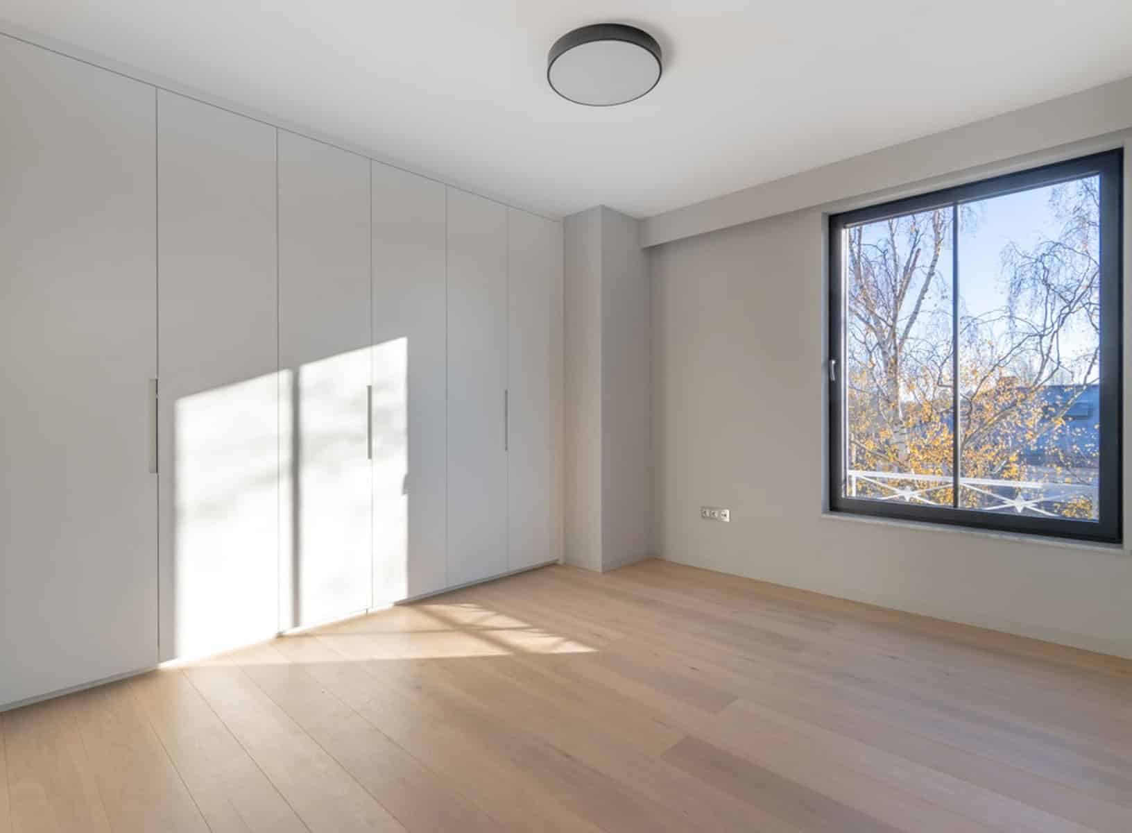 Chambre Lumineuse avec Placards – You Real Estate Agency Chambre lumineuse d’appartement avec placards intégrés, parquet clair et grande fenêtre.