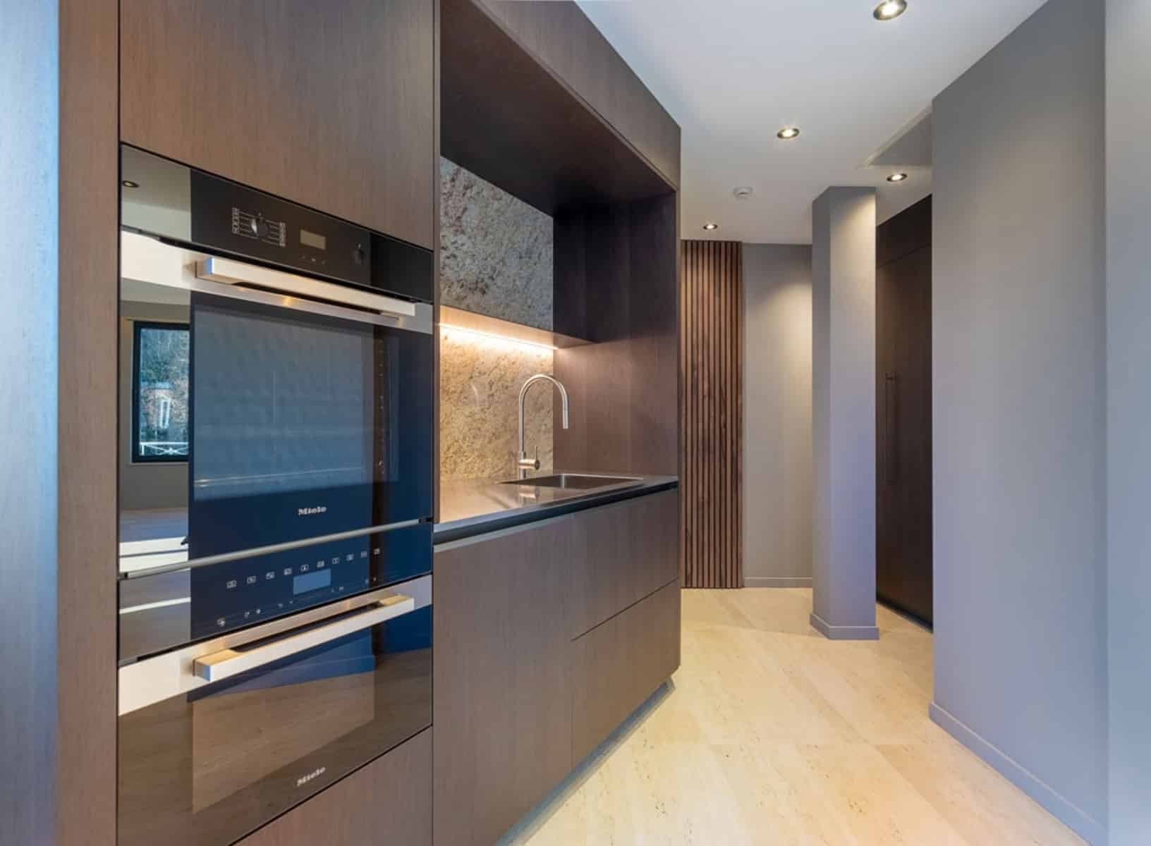 whise photo 14 Modern kitchen with built-in Miele appliances, dark wood cabinets, marble backsplash, and sleek sink under cabinet lighting.
