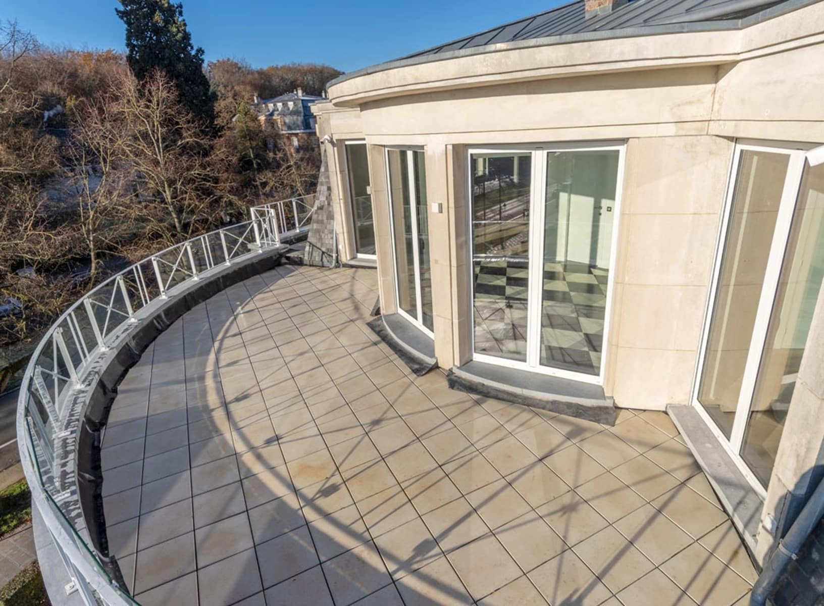 whise photo 8 Curved rooftop terrace with glass railing and large sliding doors on a beige stone building.