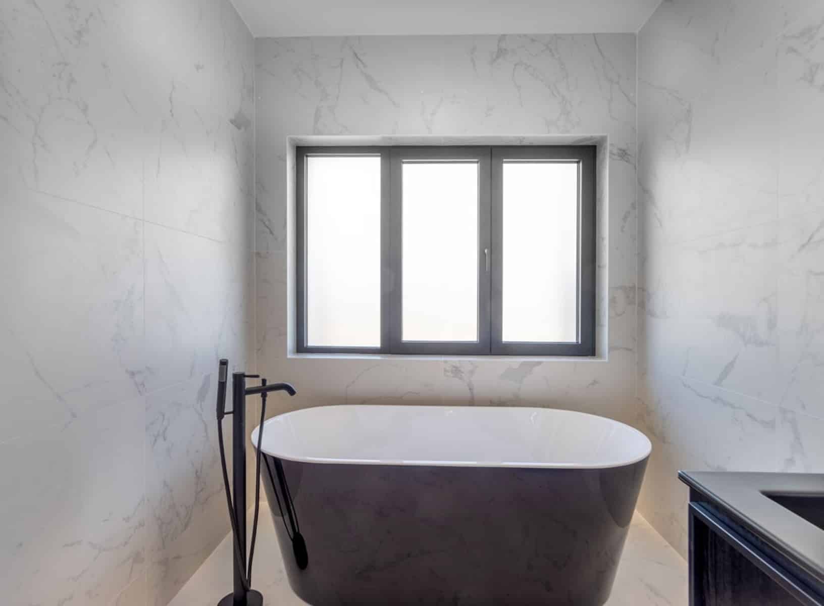 whise photo 20 Freestanding dark bathtub in a marble bathroom with a large window behind it.